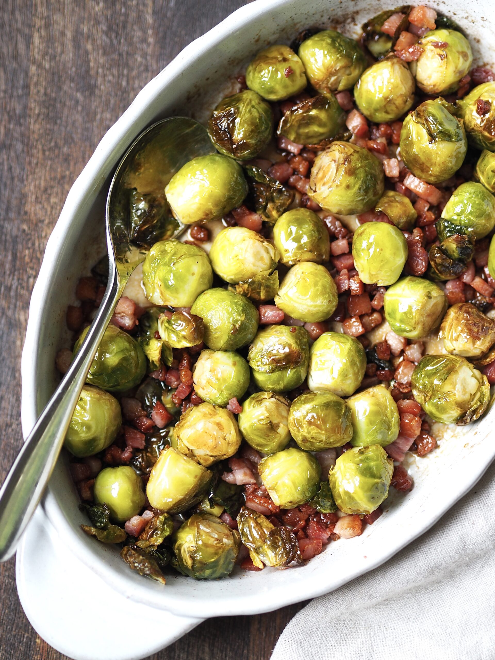 White oval serving dish of brussels sprouts with bacon pieces.