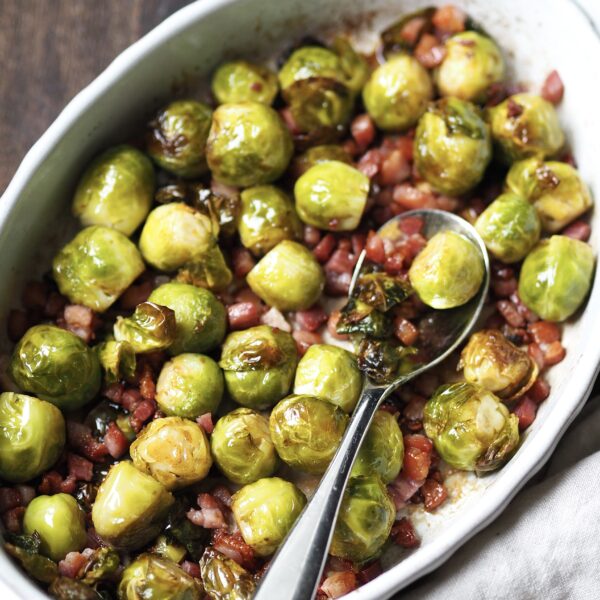 White serving dish with whole roasted sprouts with bacon lardons.