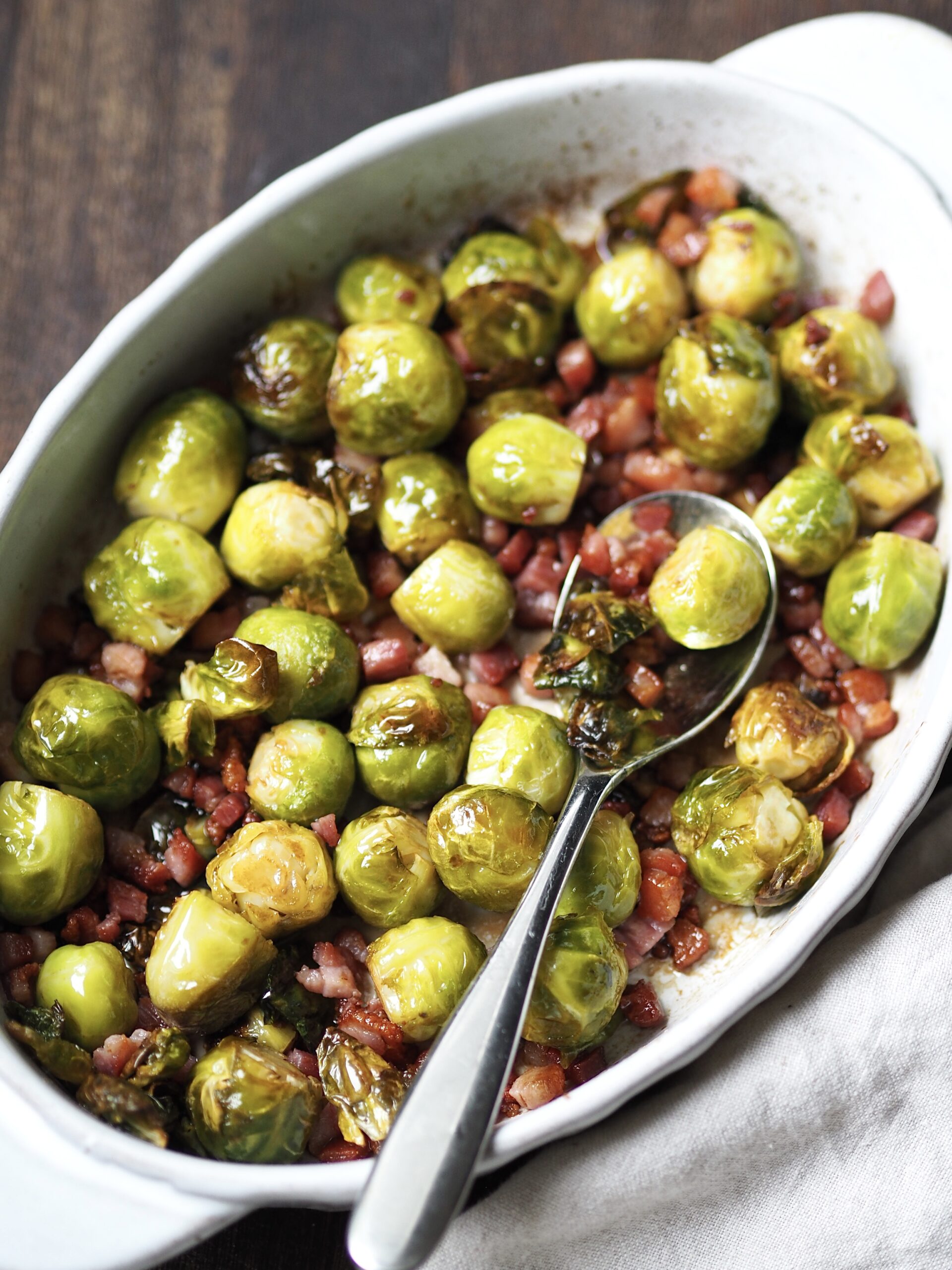 White serving dish with whole roasted sprouts with bacon lardons.