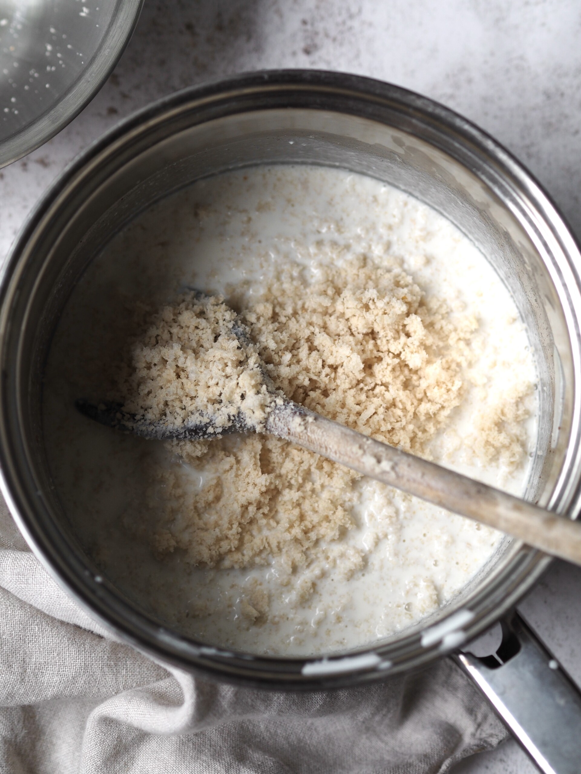 A wooden spoon stirring breadcrumbs into a pan of warm milk.