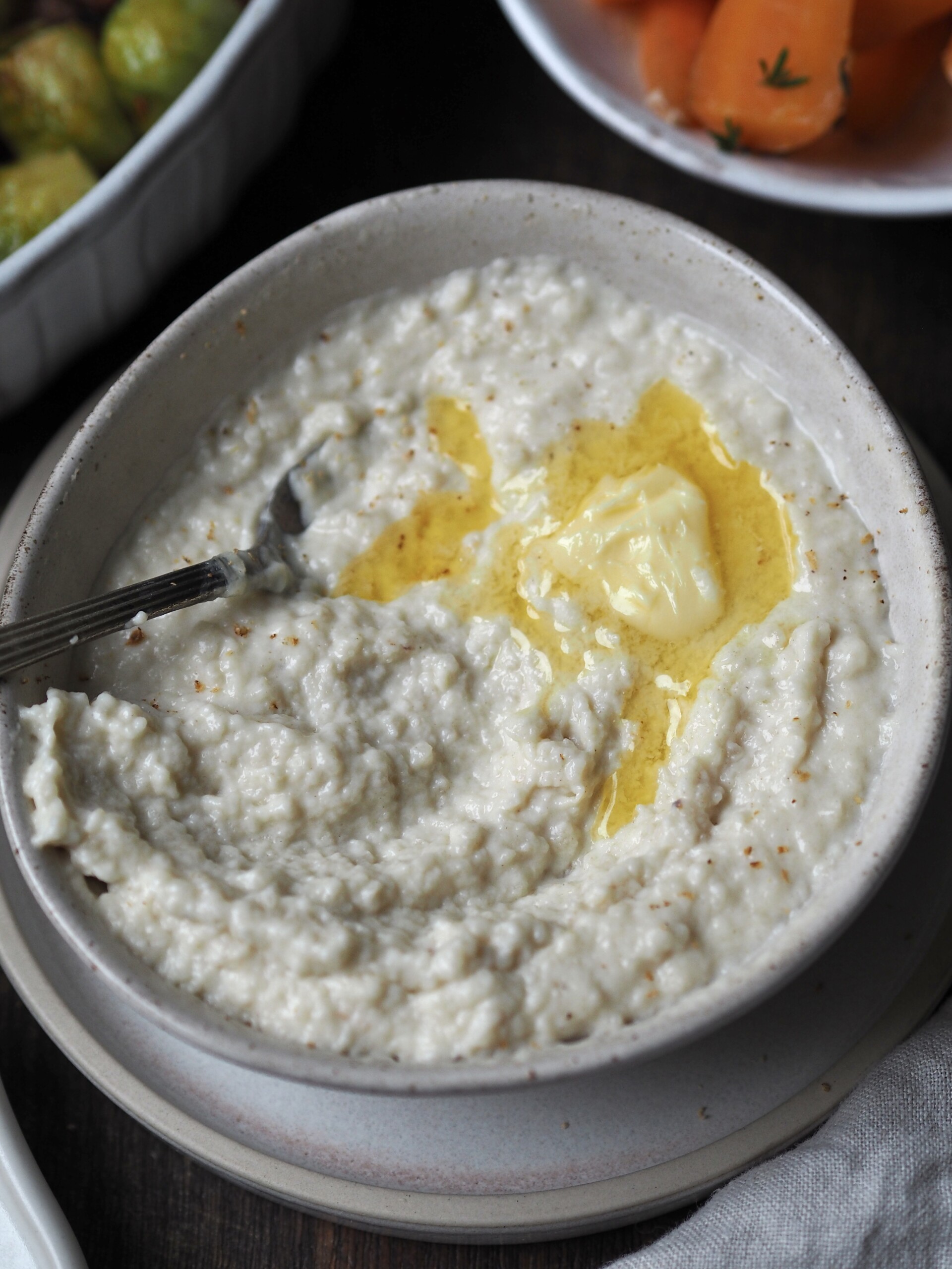 A white bowl of bread sauce topped with melted butter and grated nutmeg. 