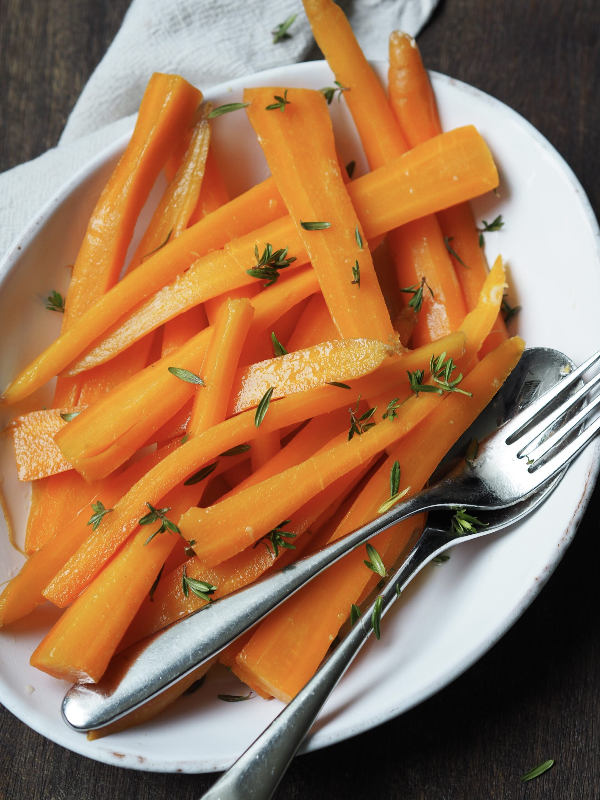 White serving dish of glazed carrots sprinkled with fresh thyme.