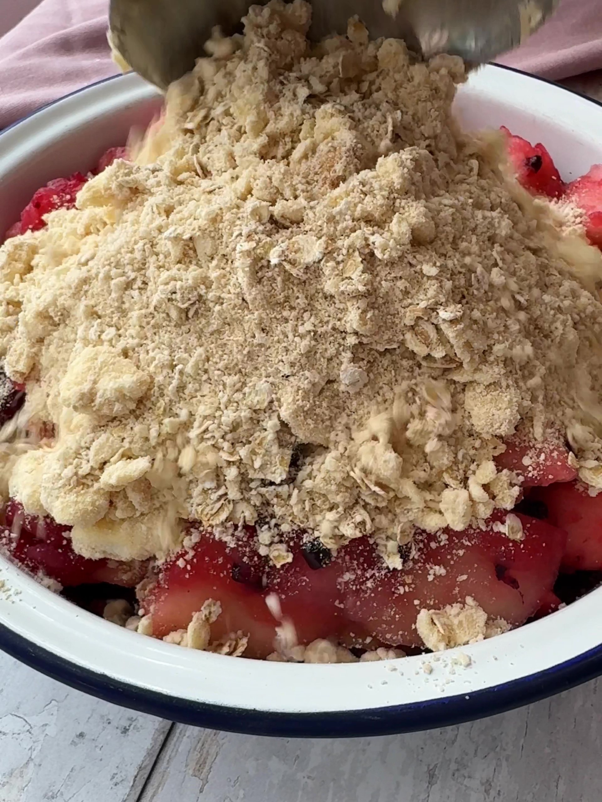 Tipping the crumble mixture over the fruit 