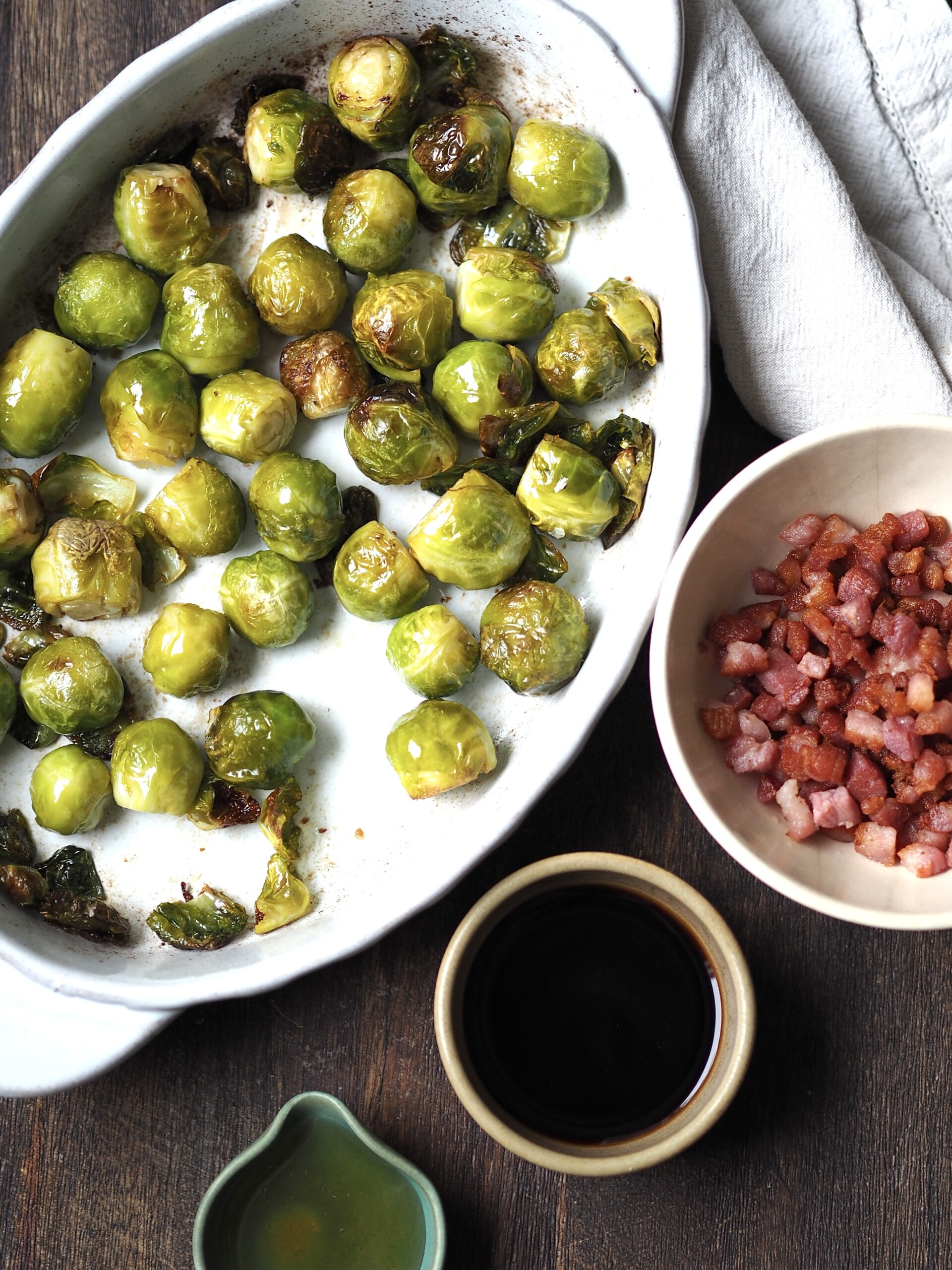 Roasted sprouts next to bowls of cooked bacon, balsamic vinegar and honey for glazing.