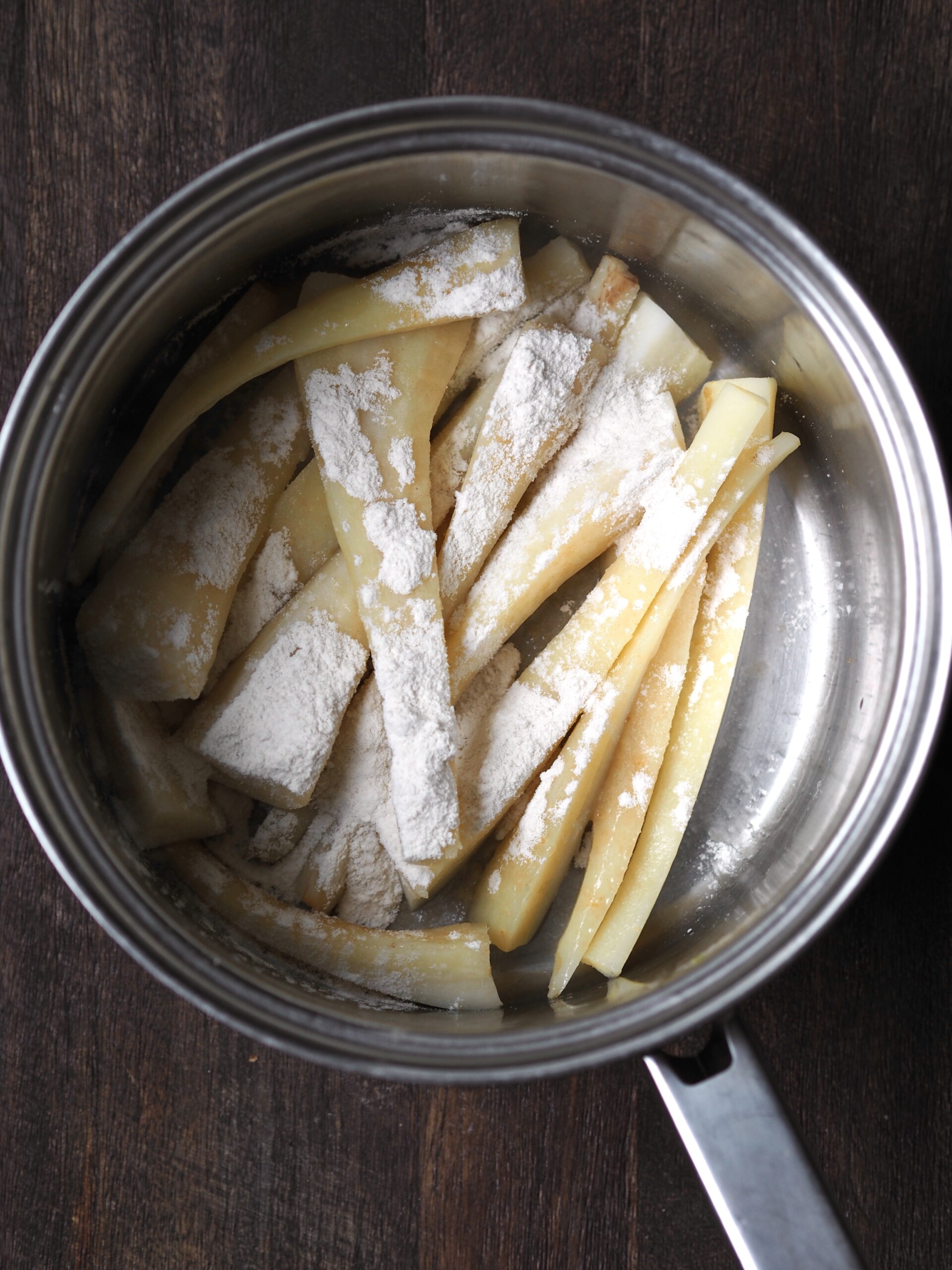 Flour sprinkled over par-boiled parsnips in a saucepan.