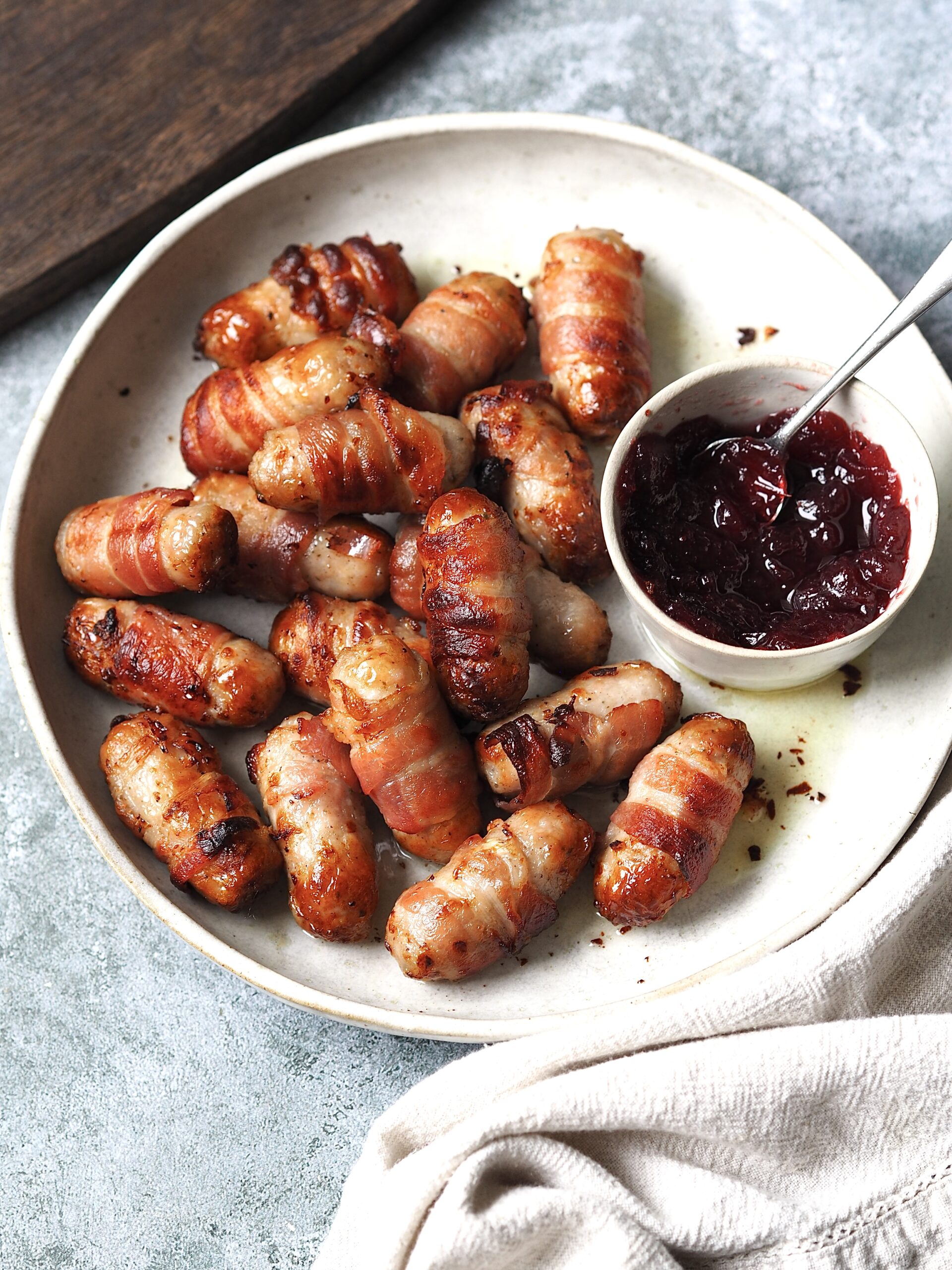 Pigs in blankets with cranberry sauce on a white serving plate.