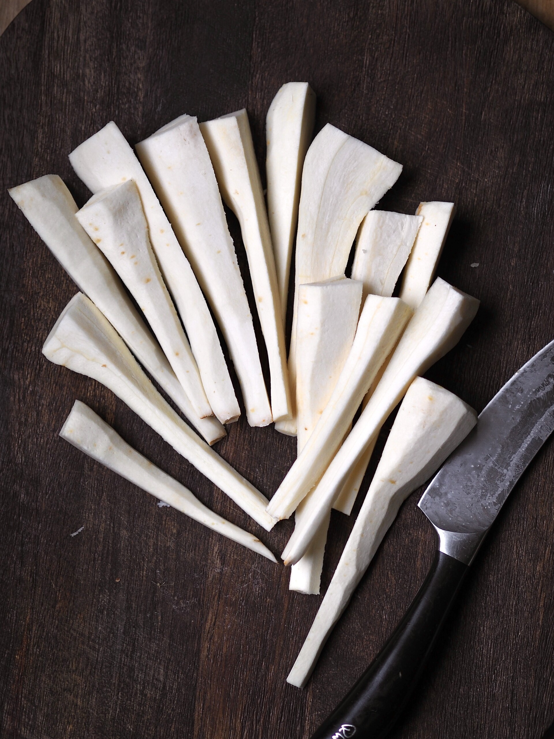 Sliced parsnips with a sharp knife on a wooden cutting board.