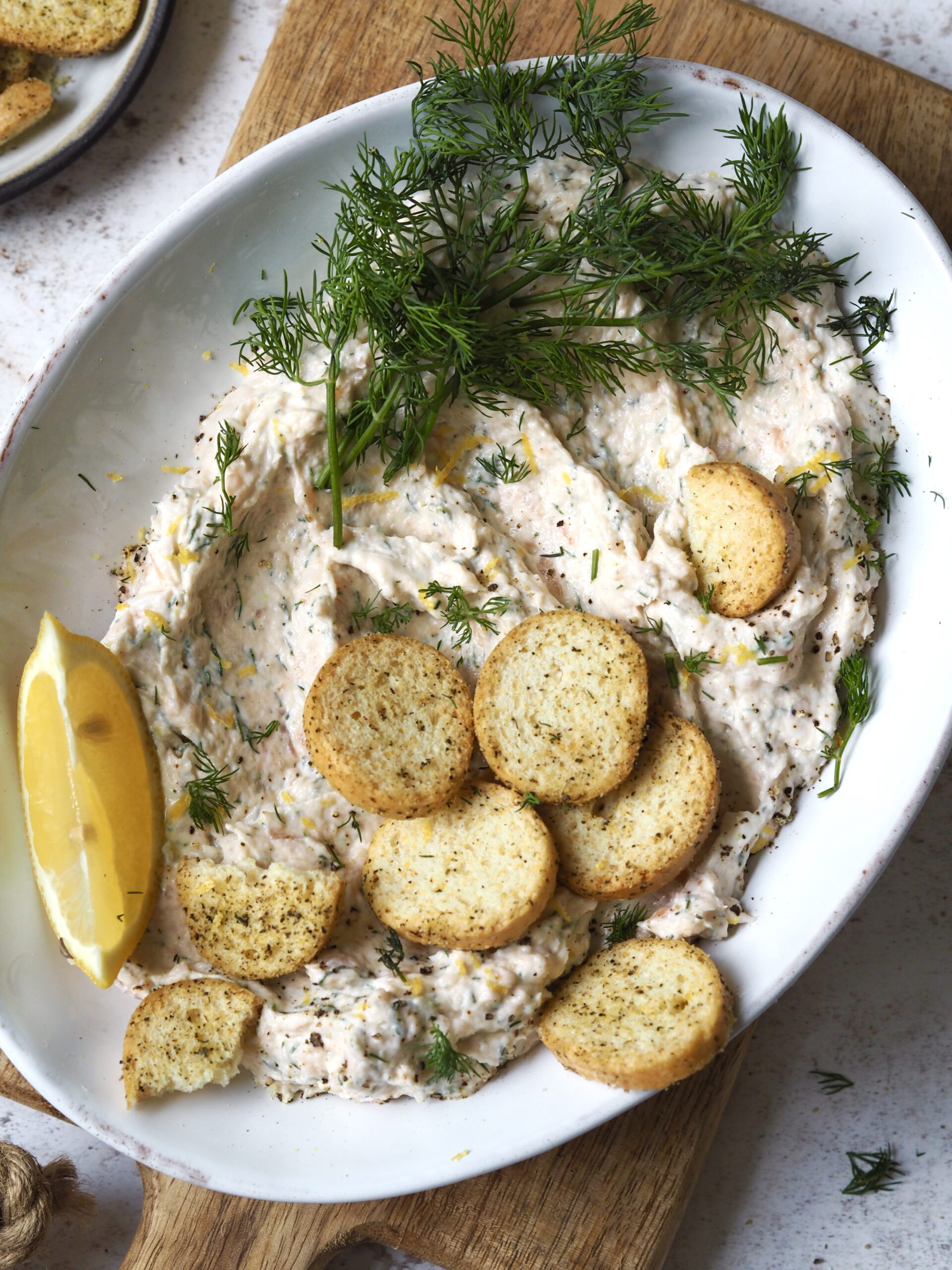 Plate of smoked salmon pate topped with fresh dill and mini crostini. 