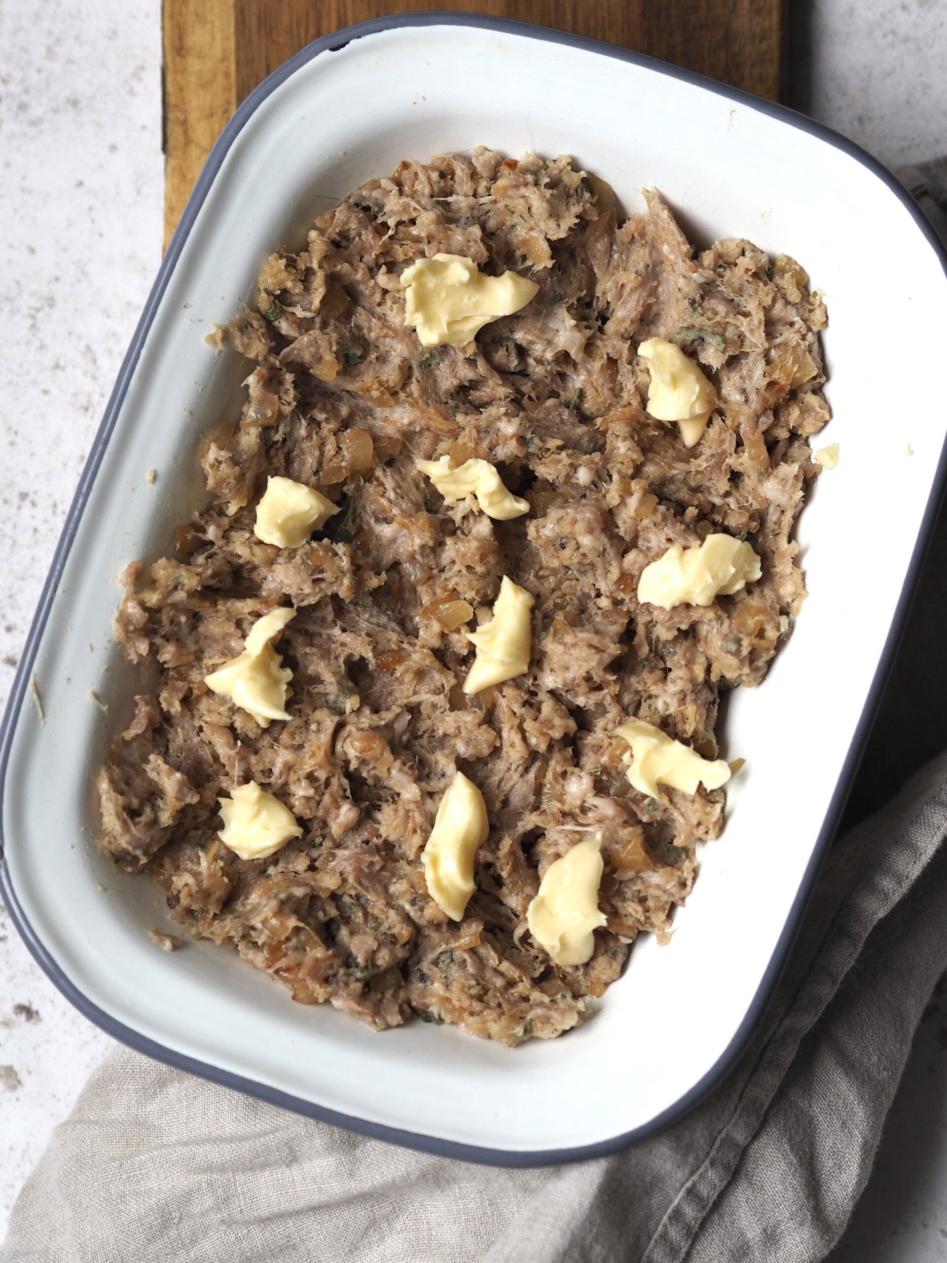 White metal baking dish of raw sausage stuffing dotted with pieces of butter.