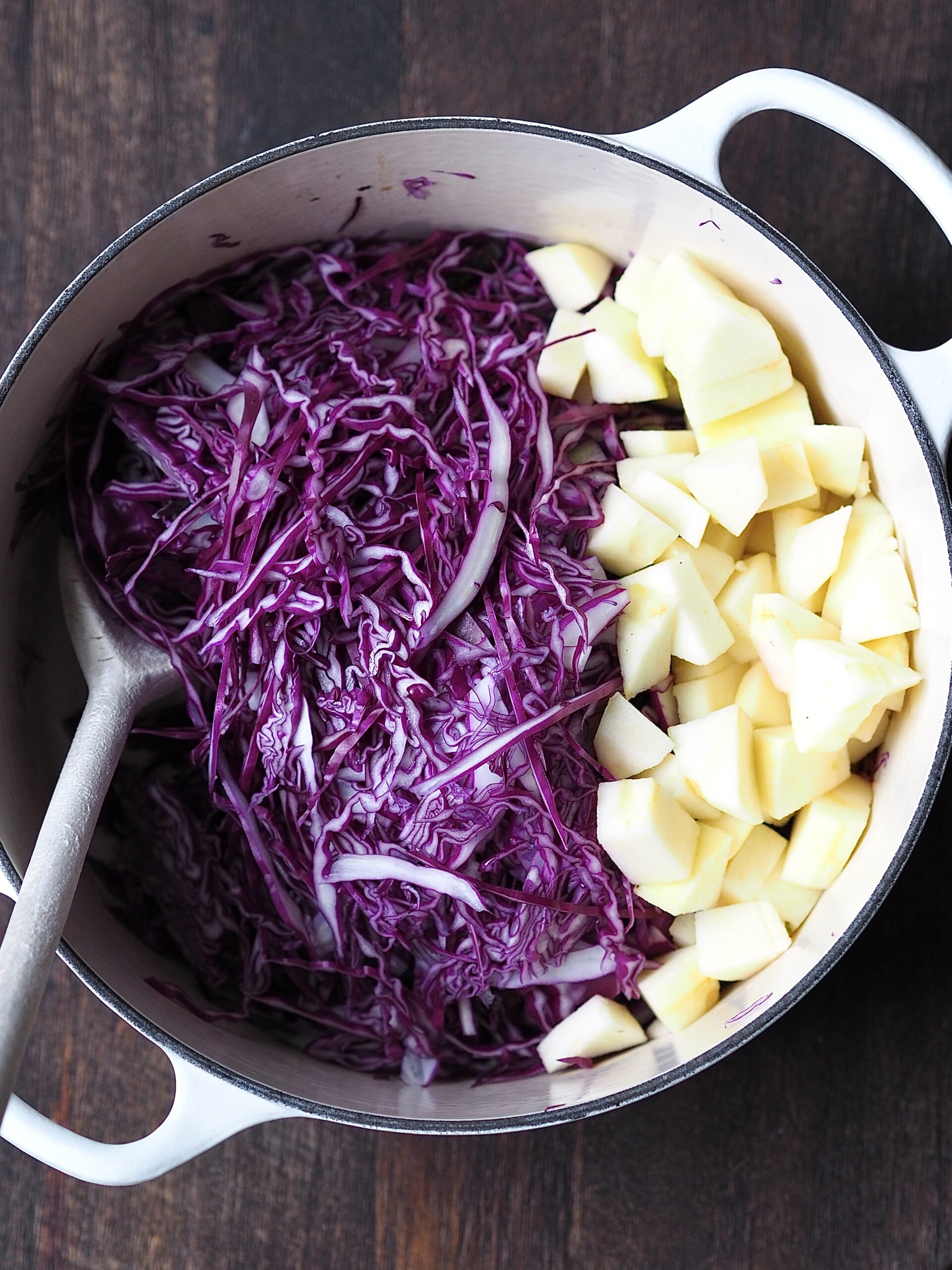 White casserole pot filled with shredded red cabbage and diced apple.