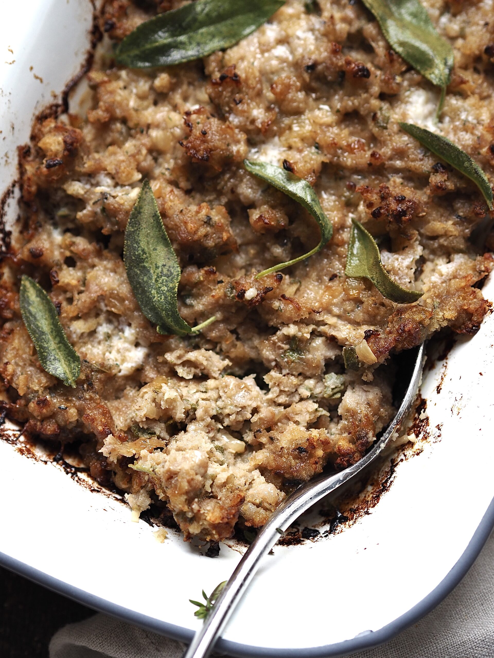 Close up of a spoon breaking into a dish of sausage stuffing. 