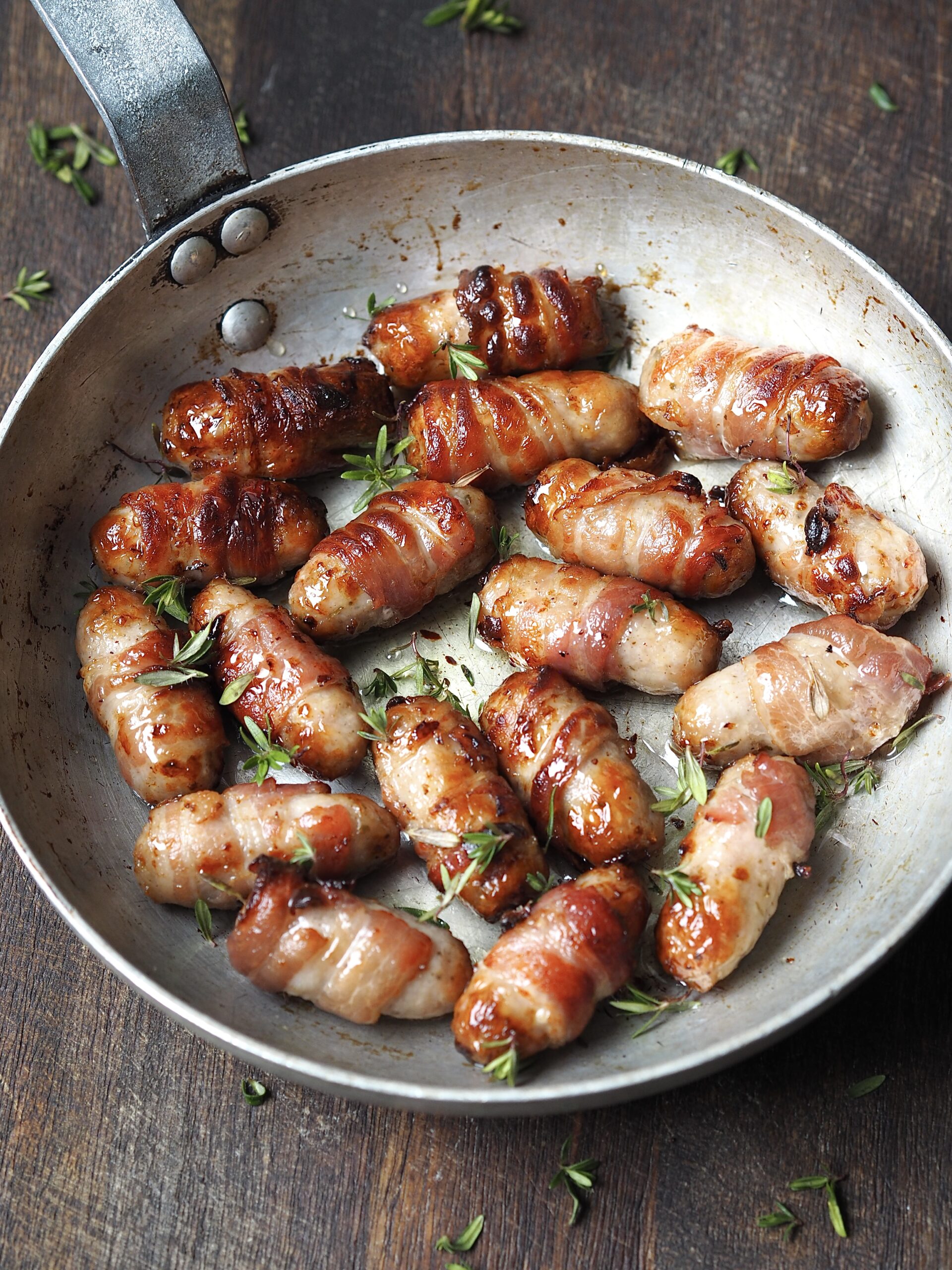 Close up of a metal frying pan of pigs in blankets in a honey and fresh thyme glaze.