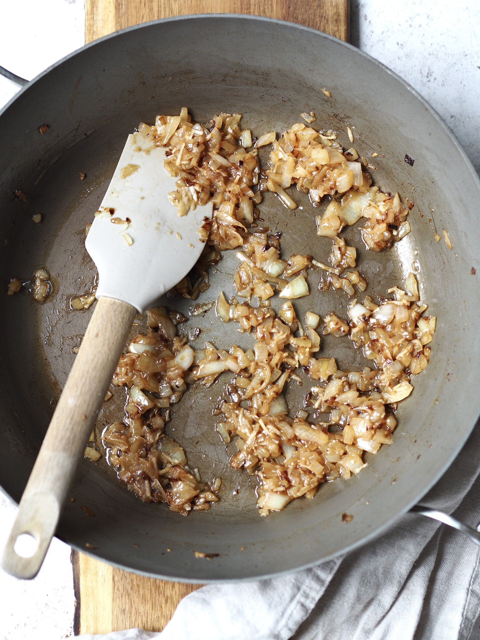 Onions bring fried in a grey frying pan.