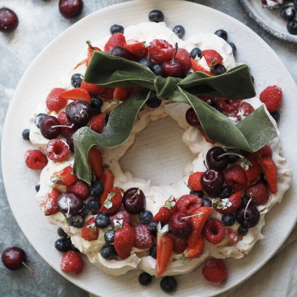 Christmas Pavlova on a plate with bowls of cherries next to it.