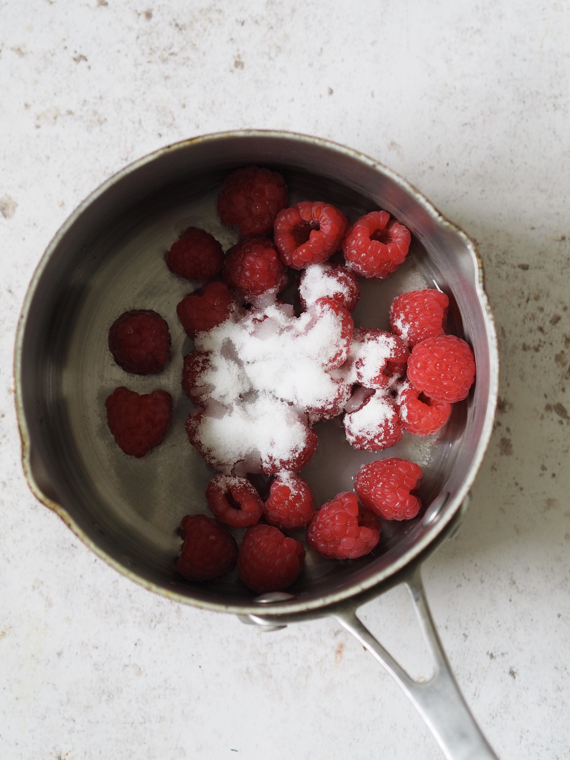 Raspberries and sugar in a sauce pan