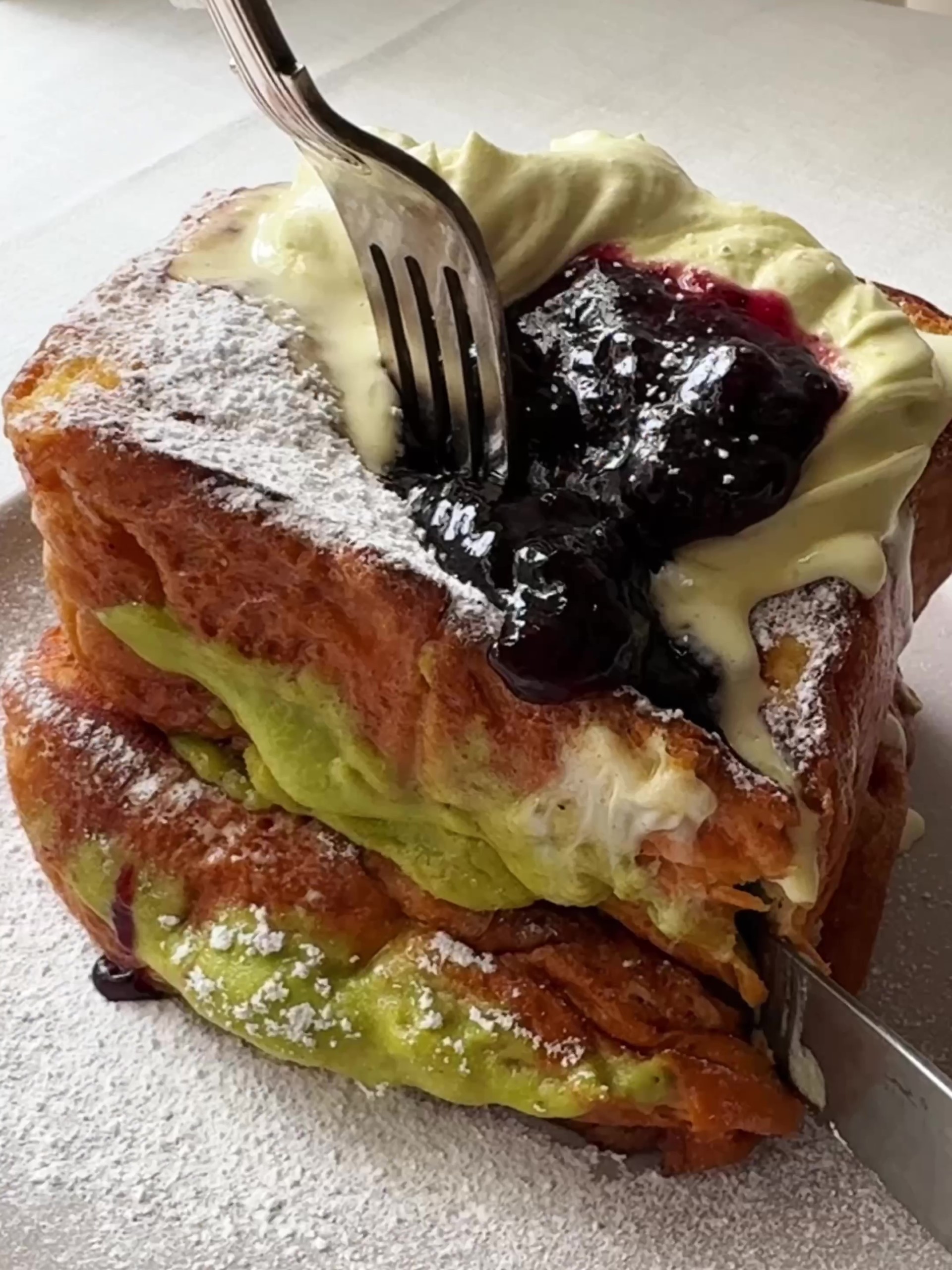 Cutting Pistachio Cream Brioche French Toast with a knife and fork