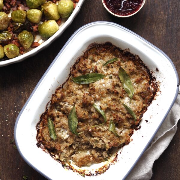 Baking dish of Sausage-Onion-Sage-Stuffing next to dishes of brussels sprouts and cranberry sauce.