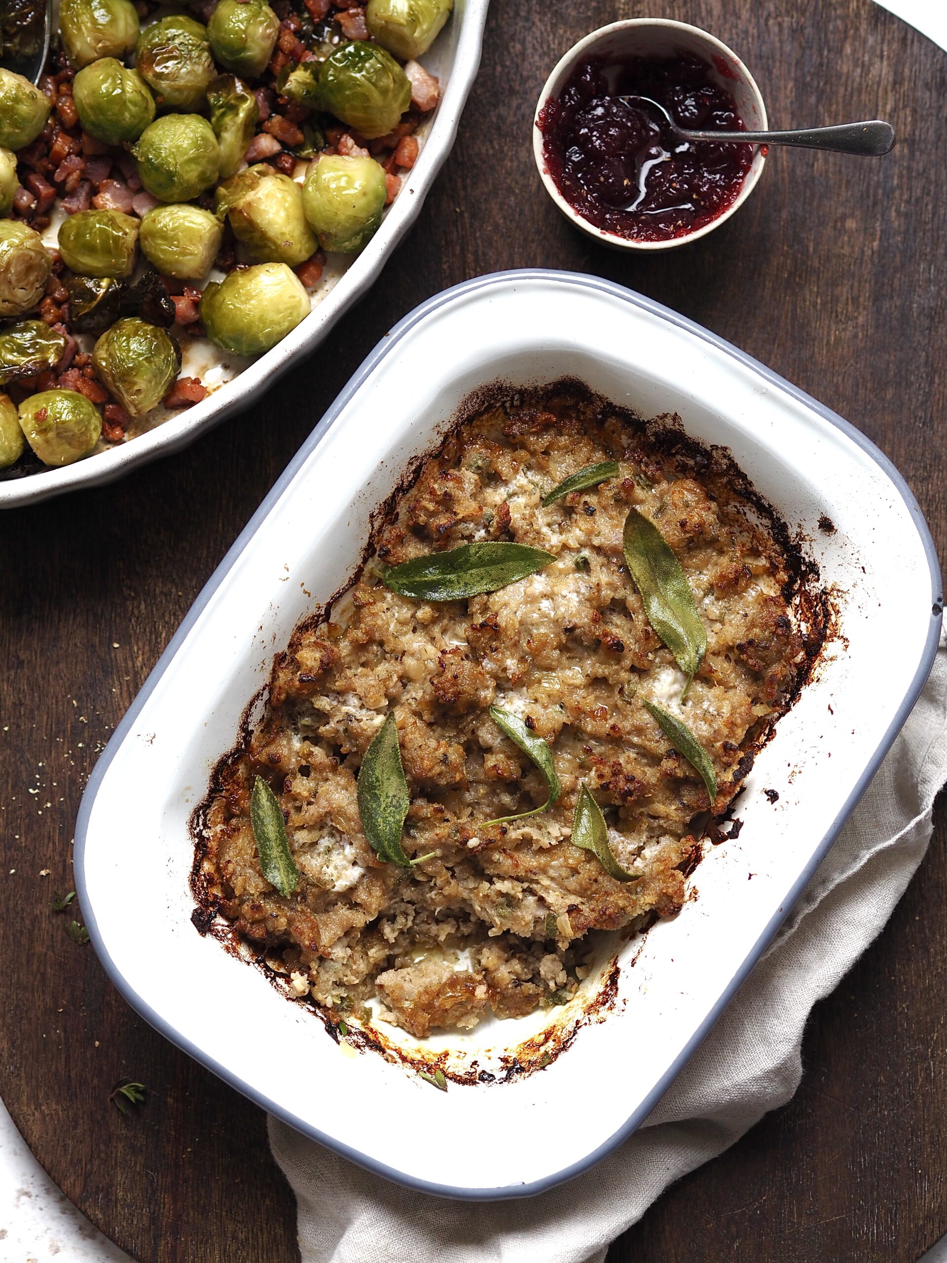 Baking dish of Sausage-Onion-Sage-Stuffing next to dishes of brussels sprouts and cranberry sauce.