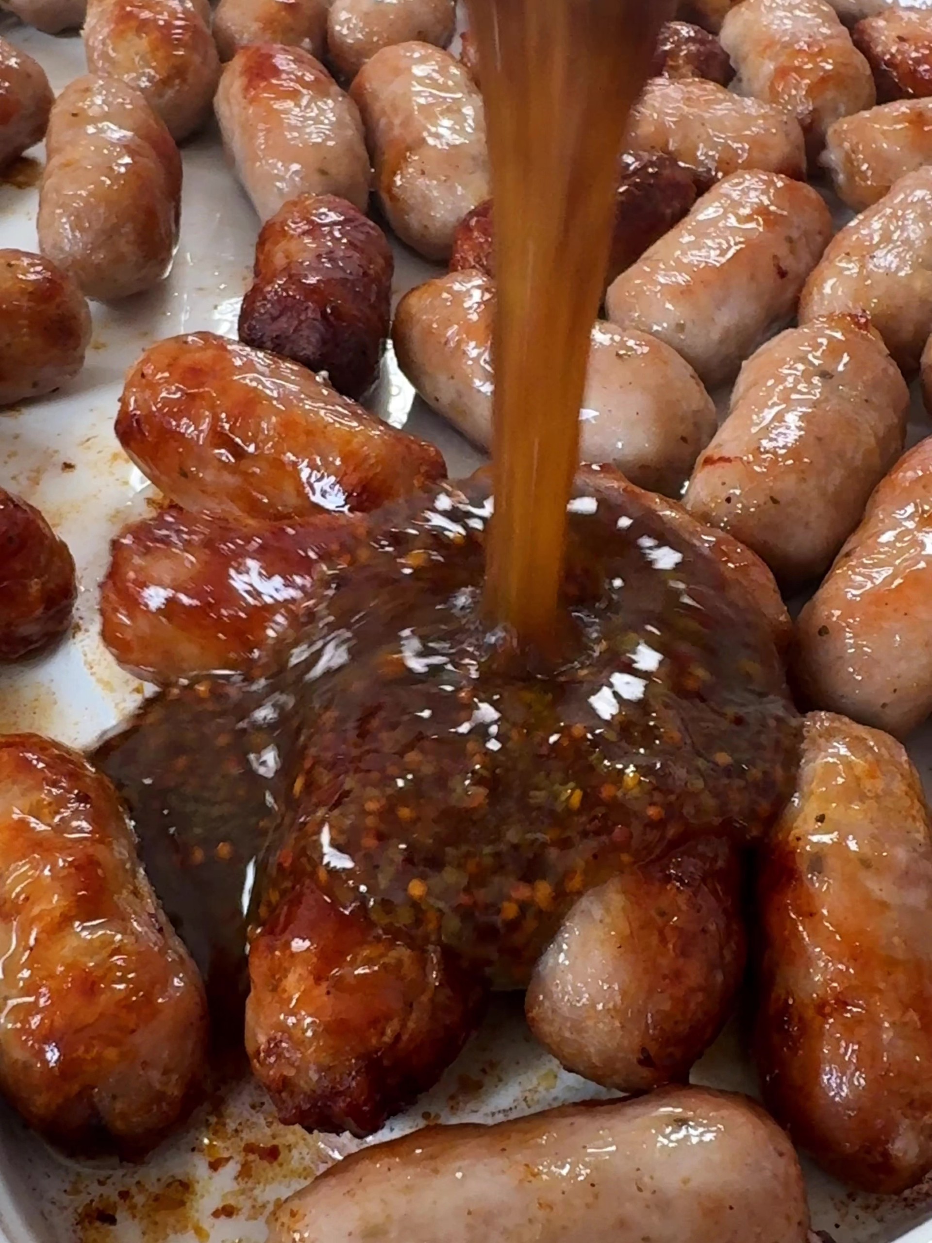 Pouring honey and mustard over the sausages.