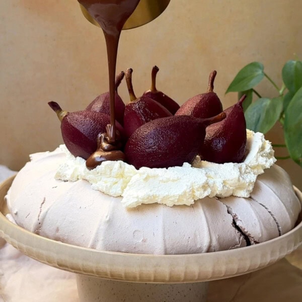 pouring chocolate over christmas pavlova with poached pears.