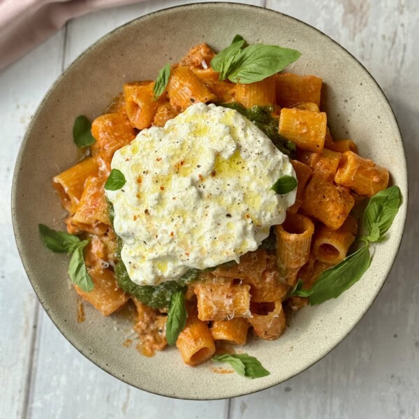 chicken and vodka pasta scooped into bowl with pesto and burrata on top.