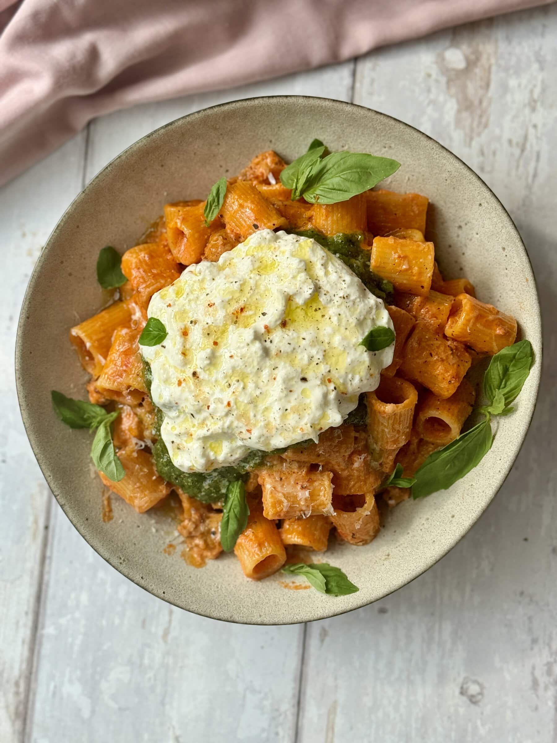 chicken and vodka pasta scooped into bowl with pesto and burrata on top.