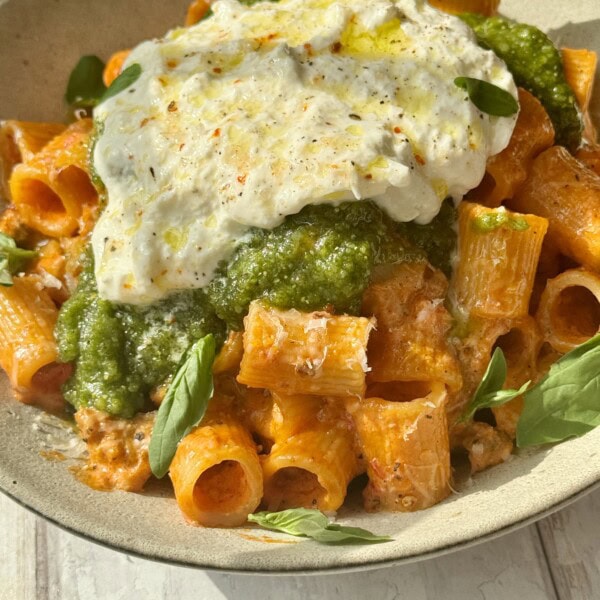 chicken and vodka pasta scooped into bowl with pesto and burrata on top.