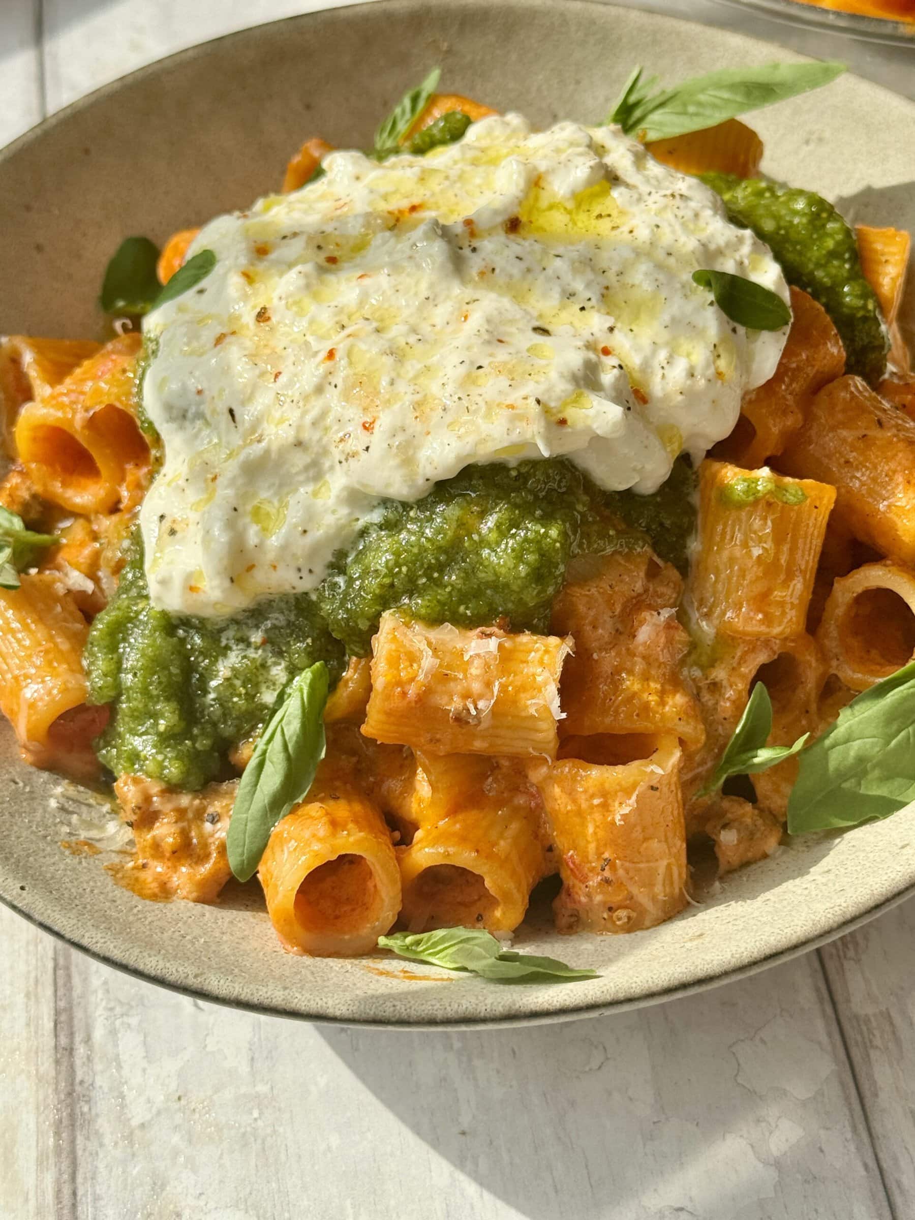 chicken and vodka pasta scooped into bowl with pesto and burrata on top.