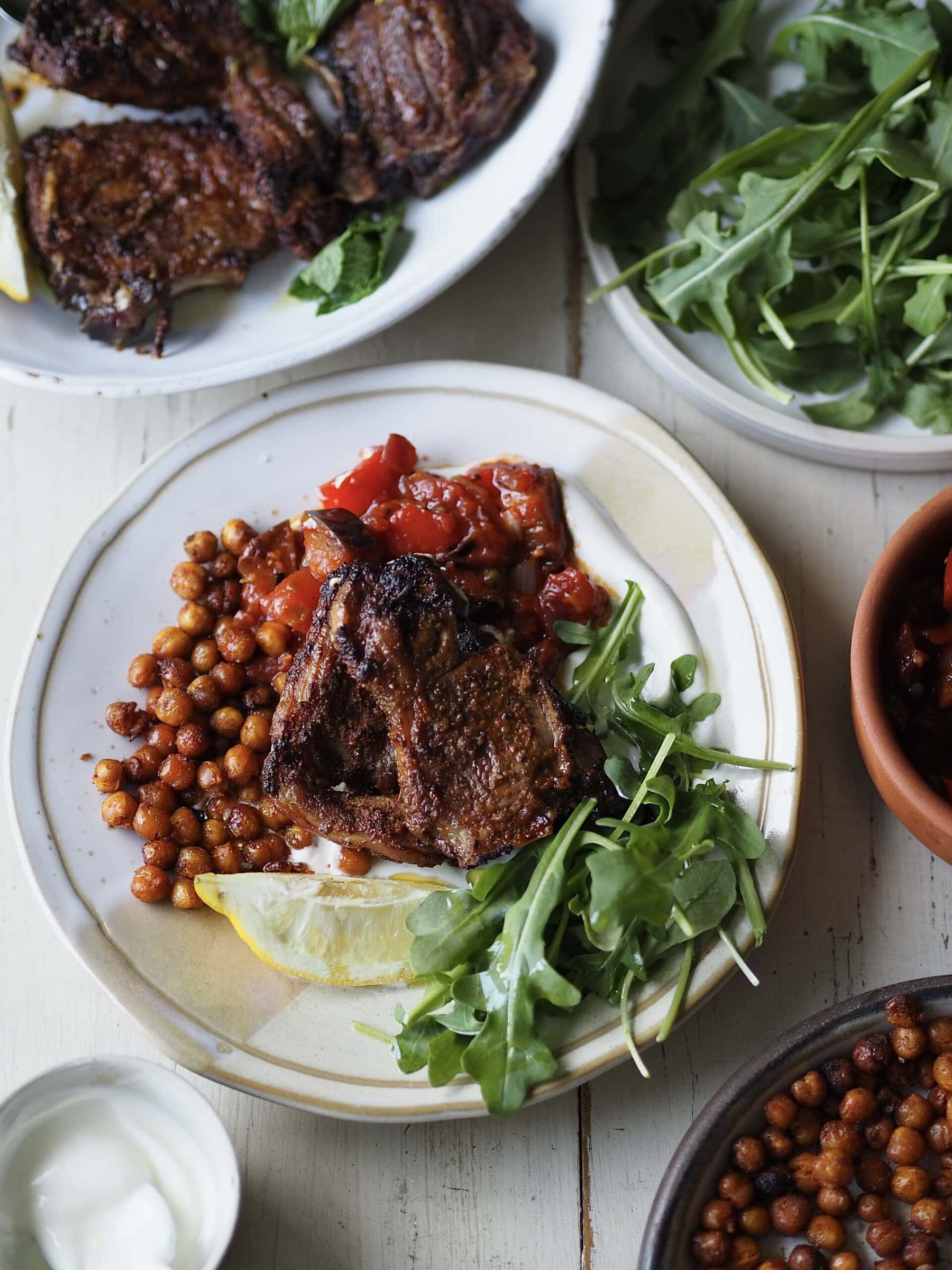 air fryer lamb chops with tomato aubergine stew and rocket on a white plate.