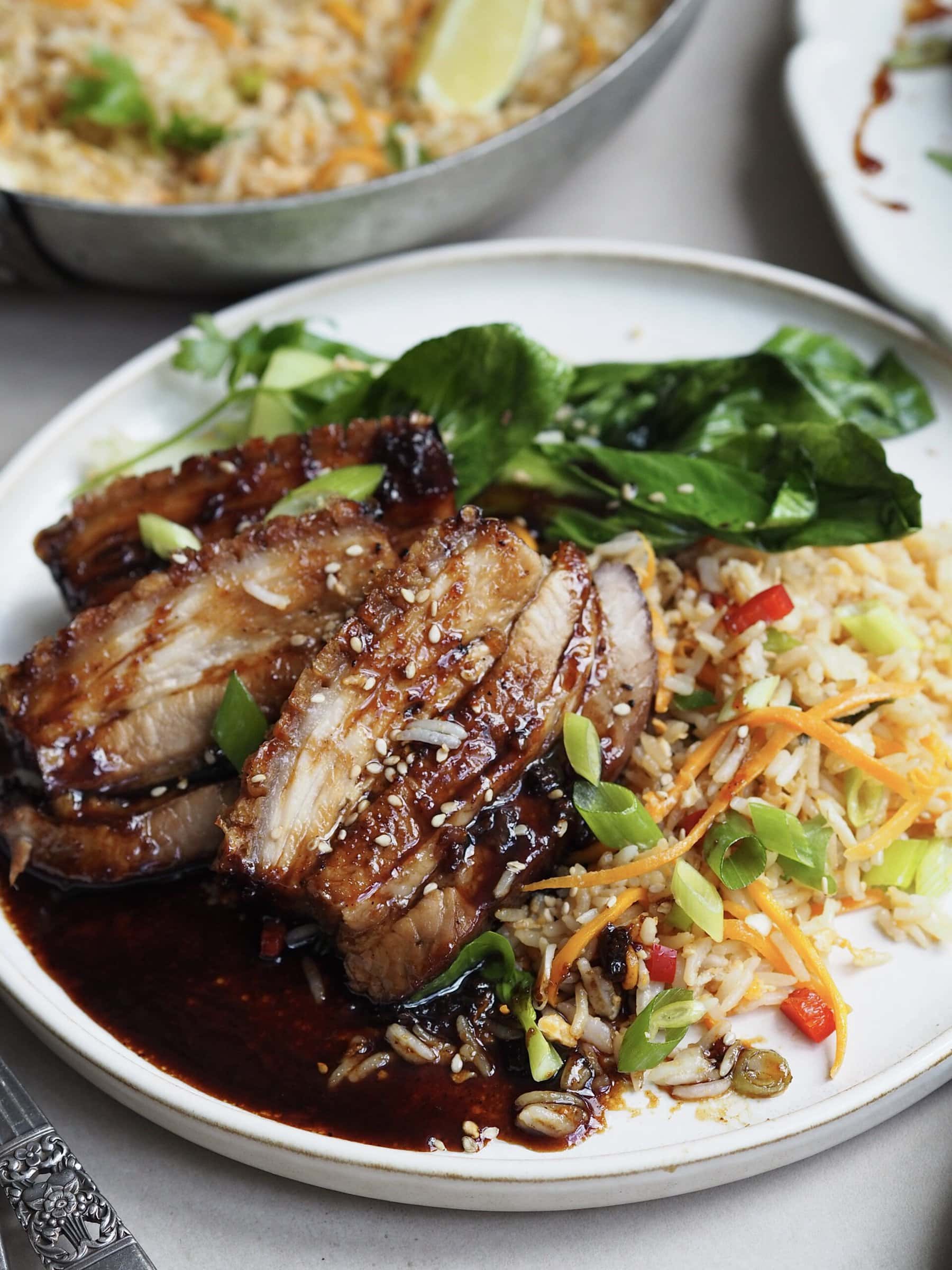 air fryer pork belly with egg fried rice and pak choi on white plate.