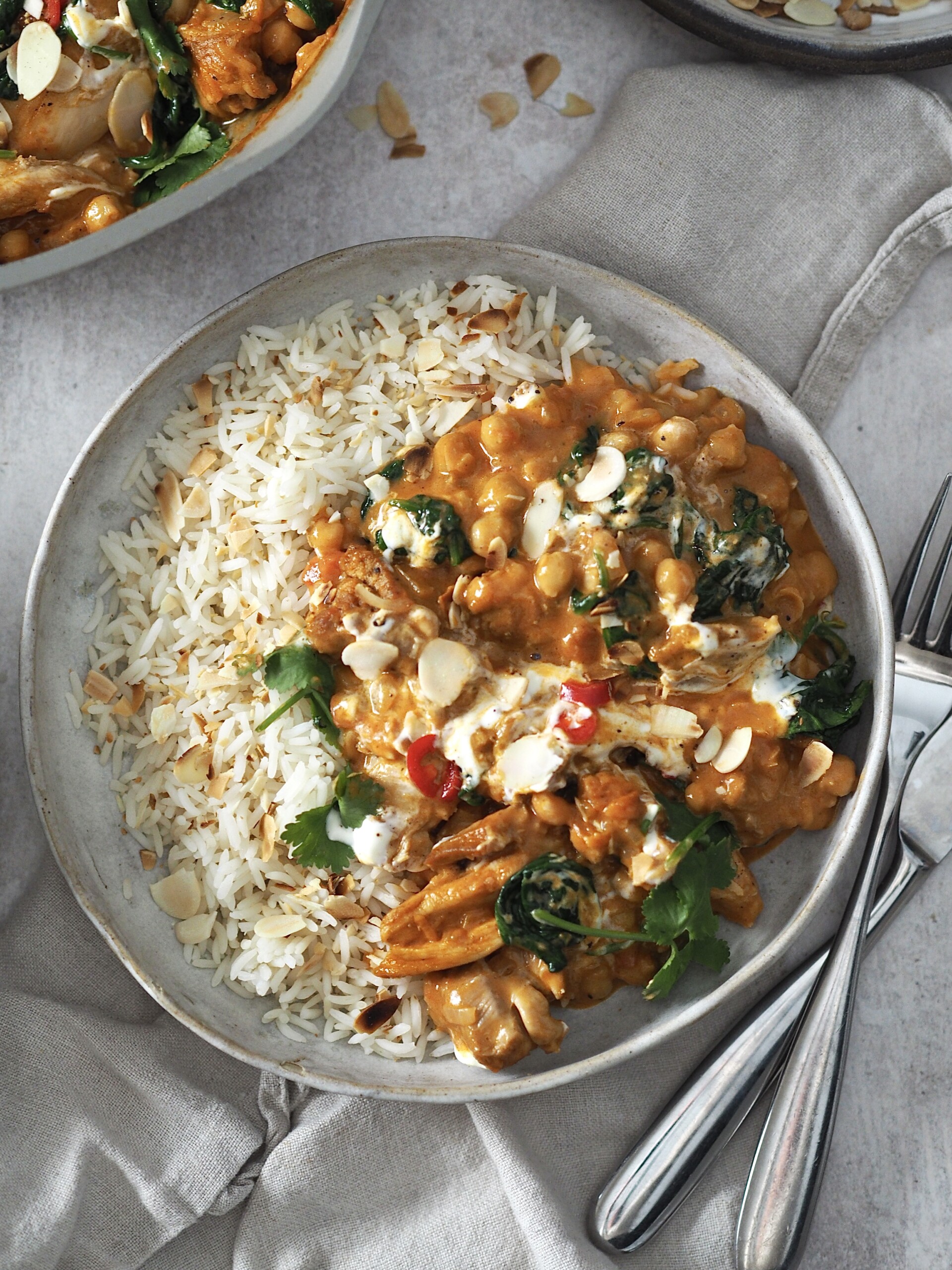 chicken and chickpea curry garnished with yoghurt and herbs served with rice.