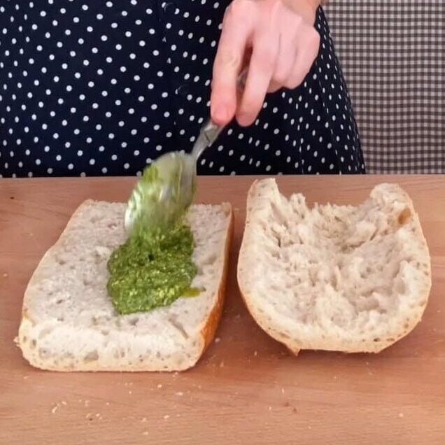 spreading pesto on the sandwich.