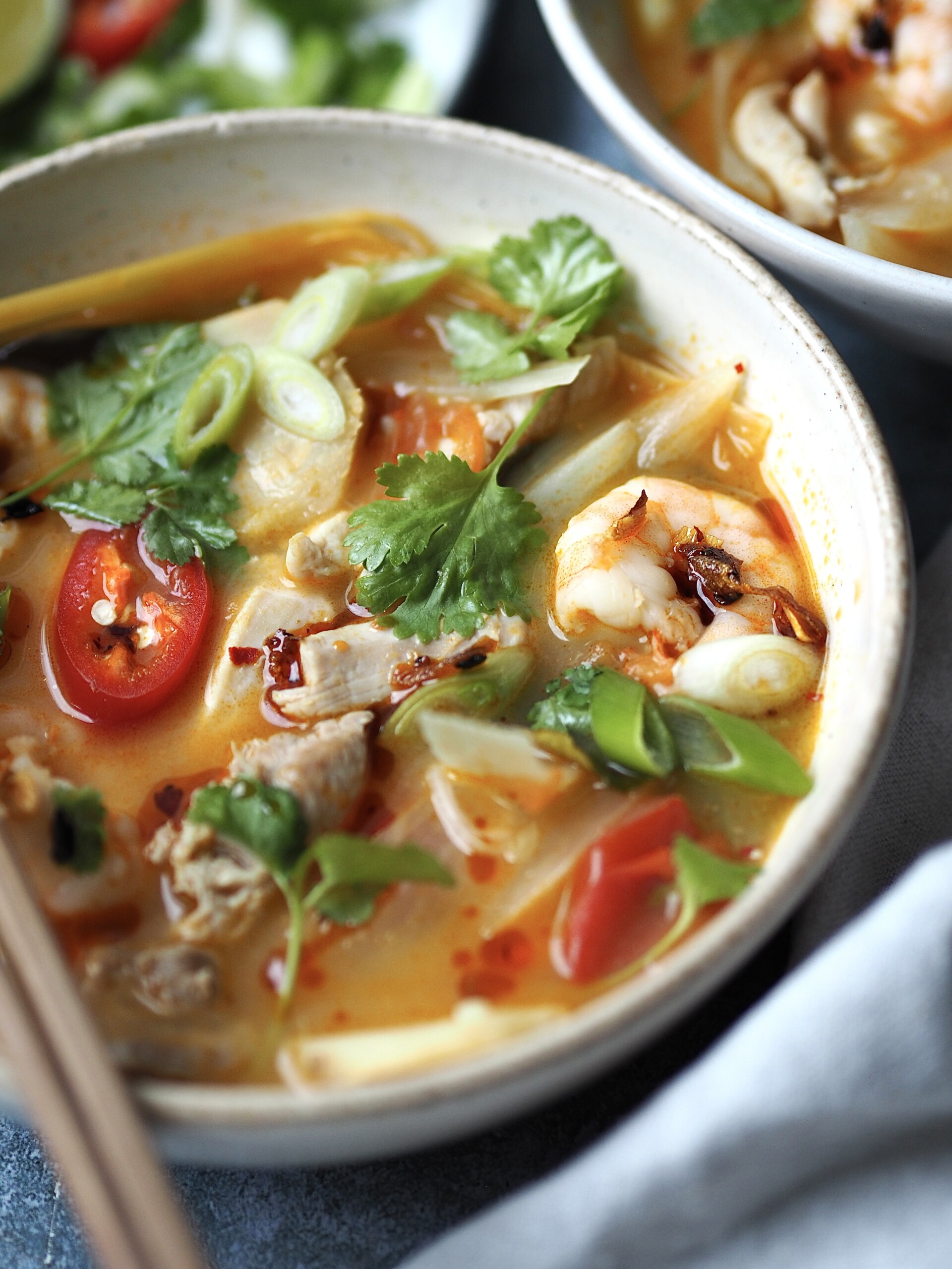 chicken tom yum soup in a white bowl with chilli and coriander on top.