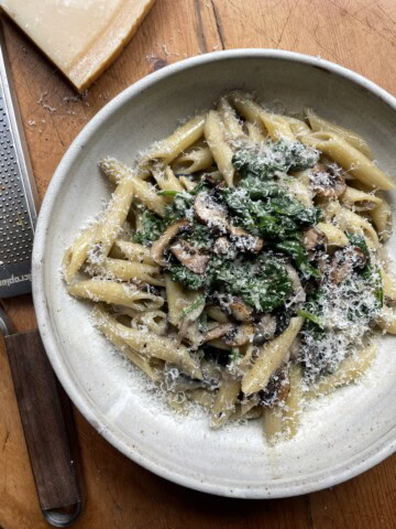 creamy mushroom and spinach pasta in a grey bowl with parmesan rind next to the bowl.