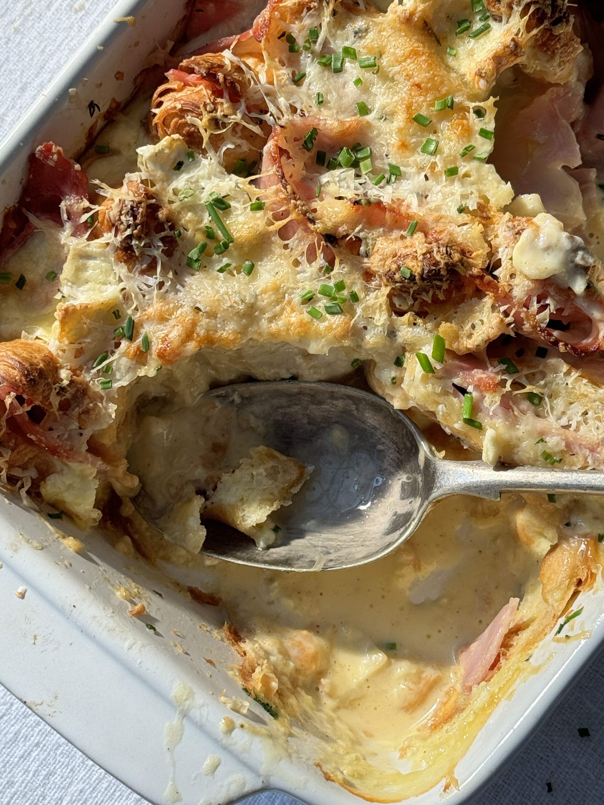 ham and cheese croissant bake with spoon and portion removed.