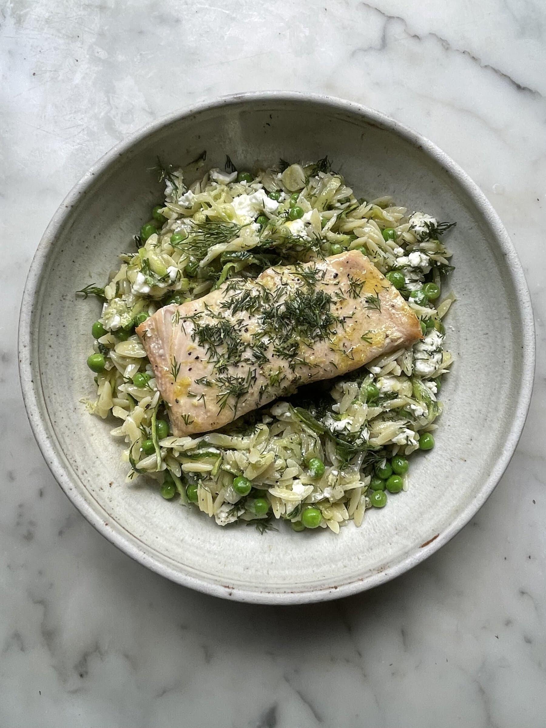 lemon orzo with feta topped with salmon in a grey bowl.