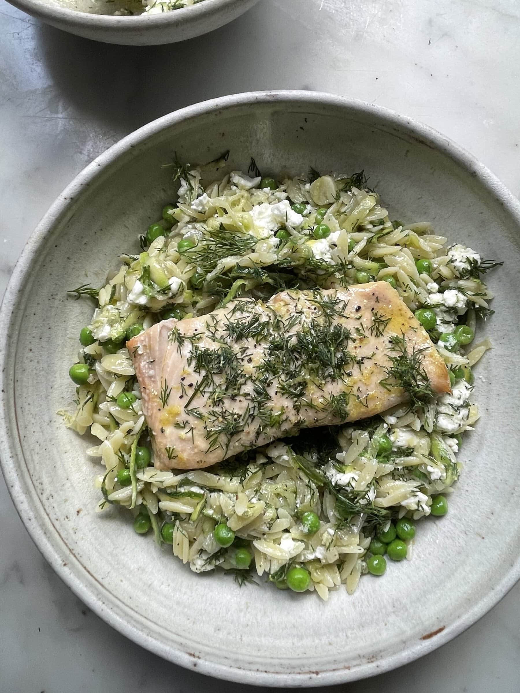 lemon orzo with feta topped with salmon in a grey bowl.