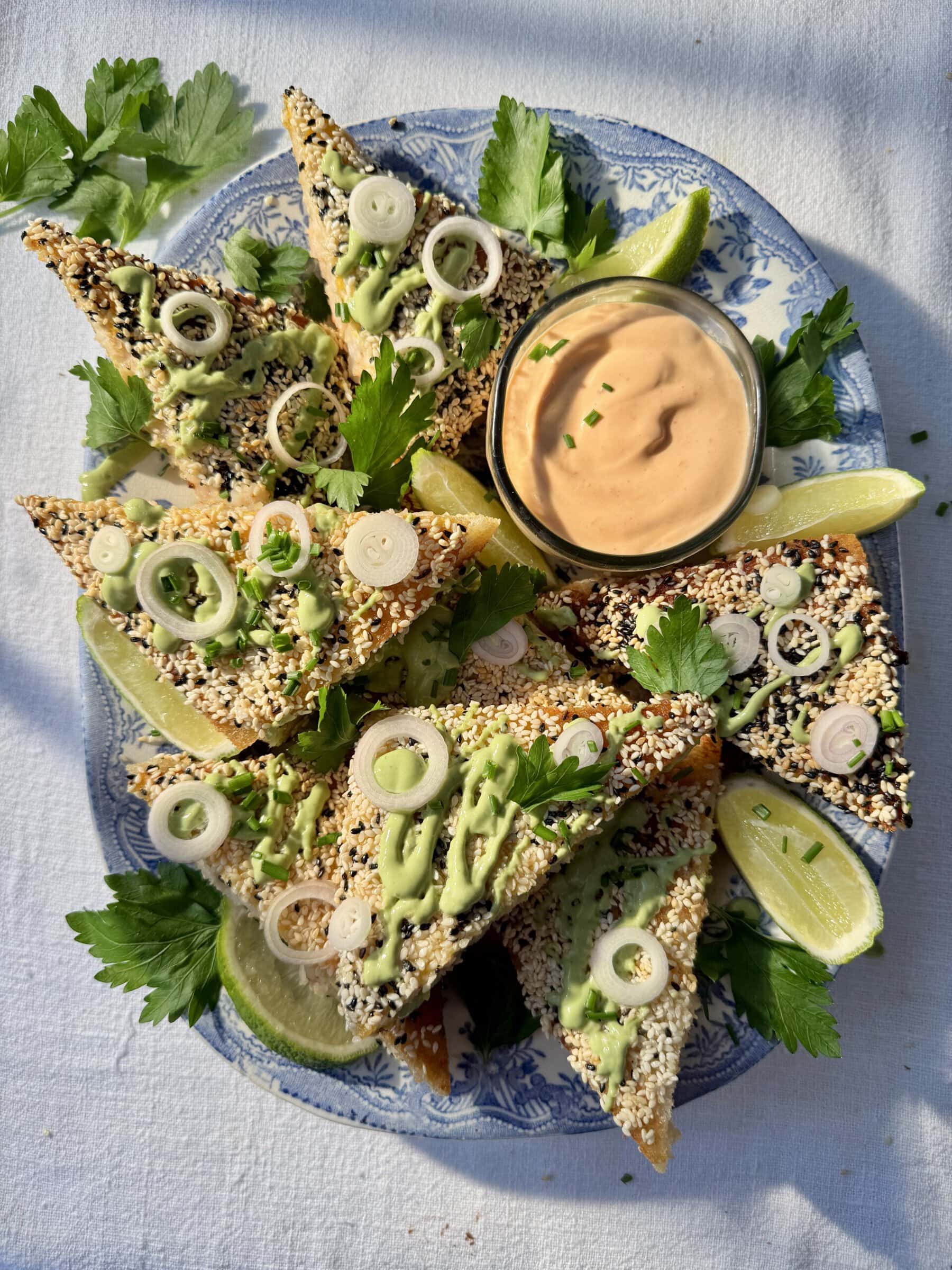 sesame prawn toast on a platter with green sauce and lime.