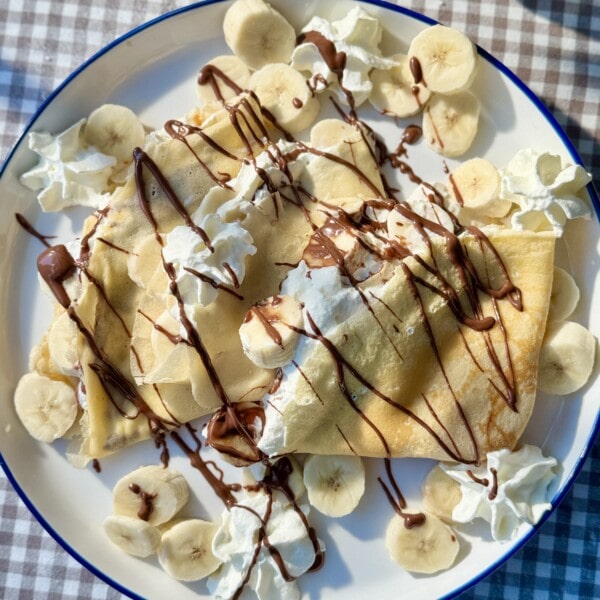 banana crepes on a plate with whipped cream and melted nutella.