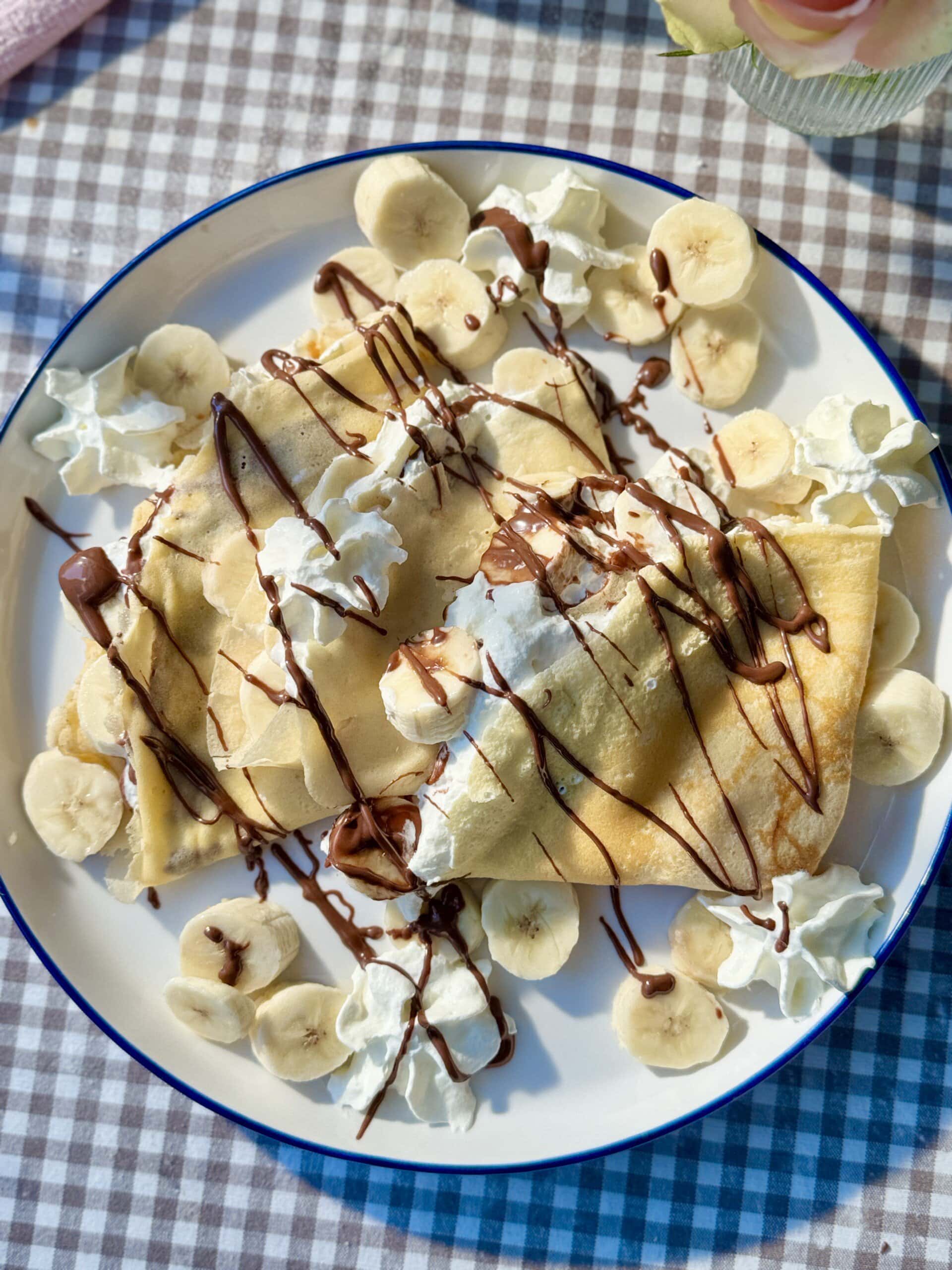 banana crepes on a plate with whipped cream and melted nutella.