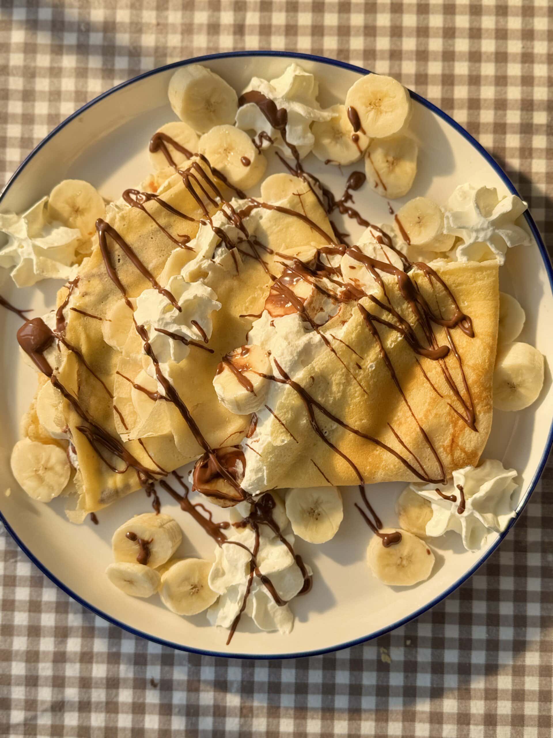 banana crepes on a plate with whipped cream and melted nutella.