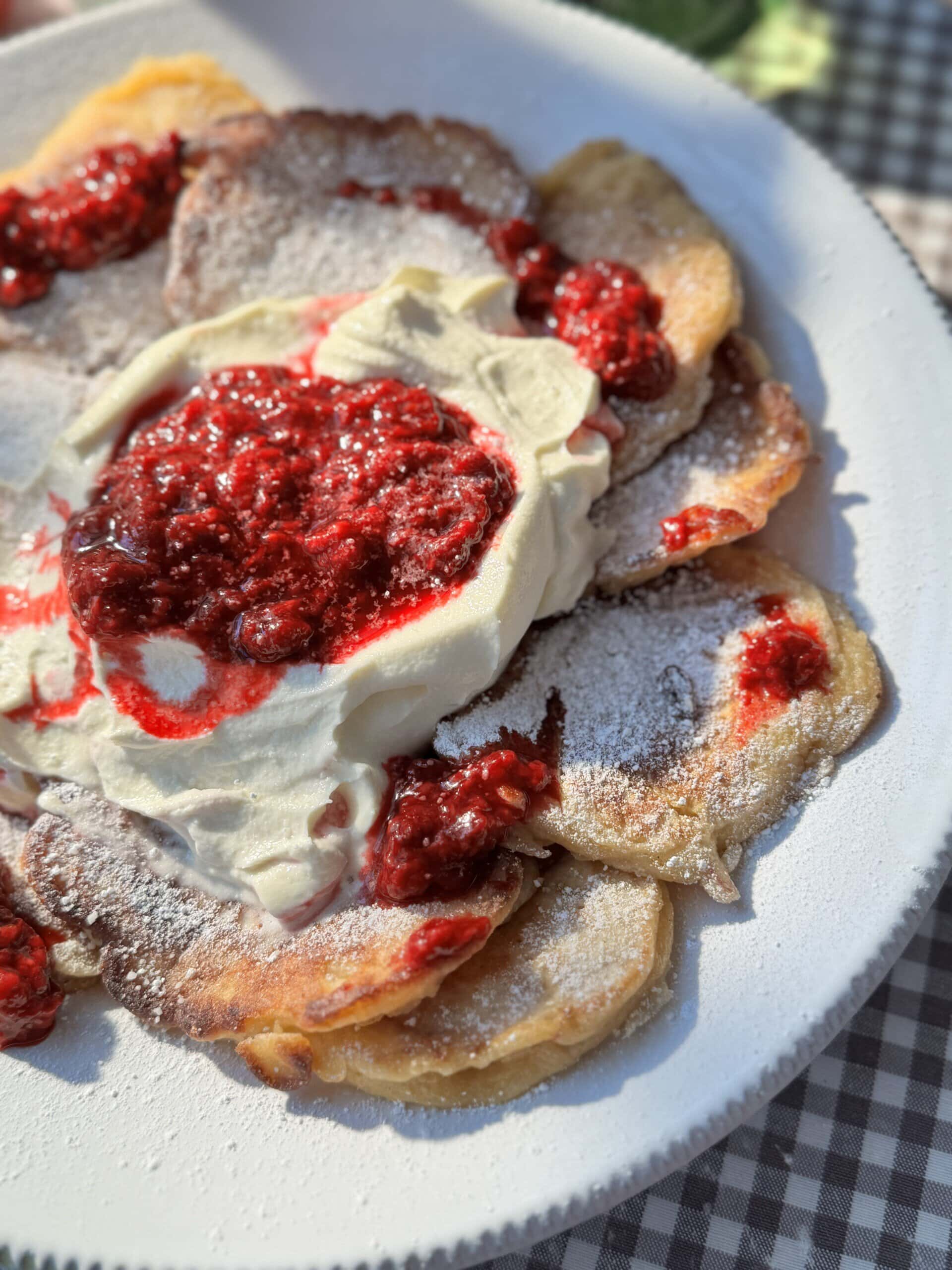 racuchy on a white plate with raspberry compote and whipped cream.