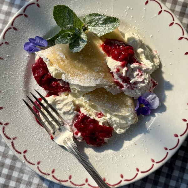 berry crepes on a white plate with raspberries and whipped cheesecake cream.