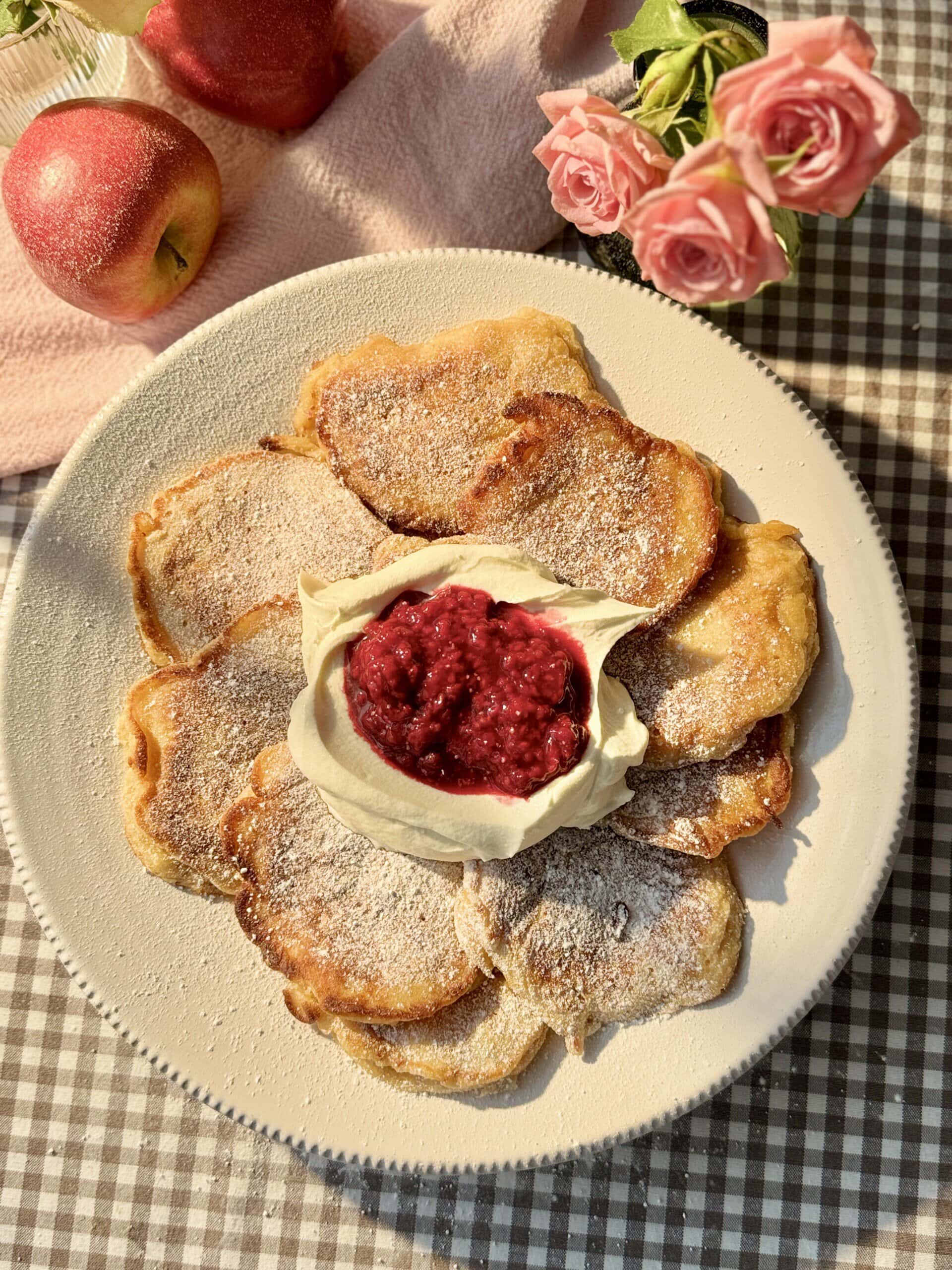 racuchy on a white plate with raspberry compote and whipped cream.