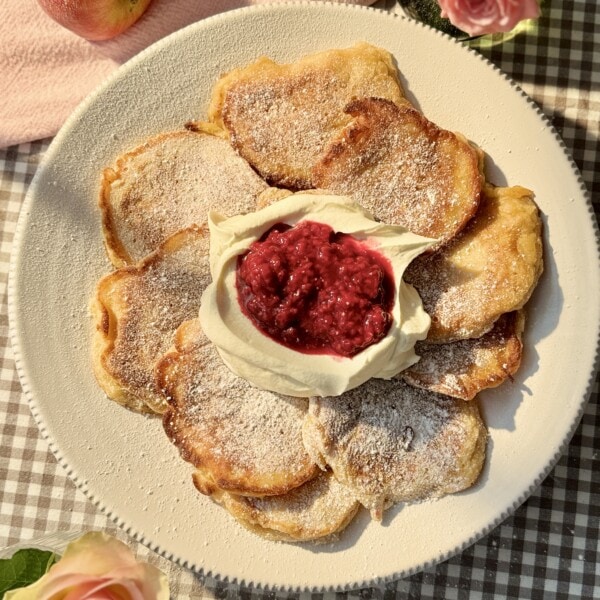 racuchy on a white plate with raspberry compote and whipped cream.