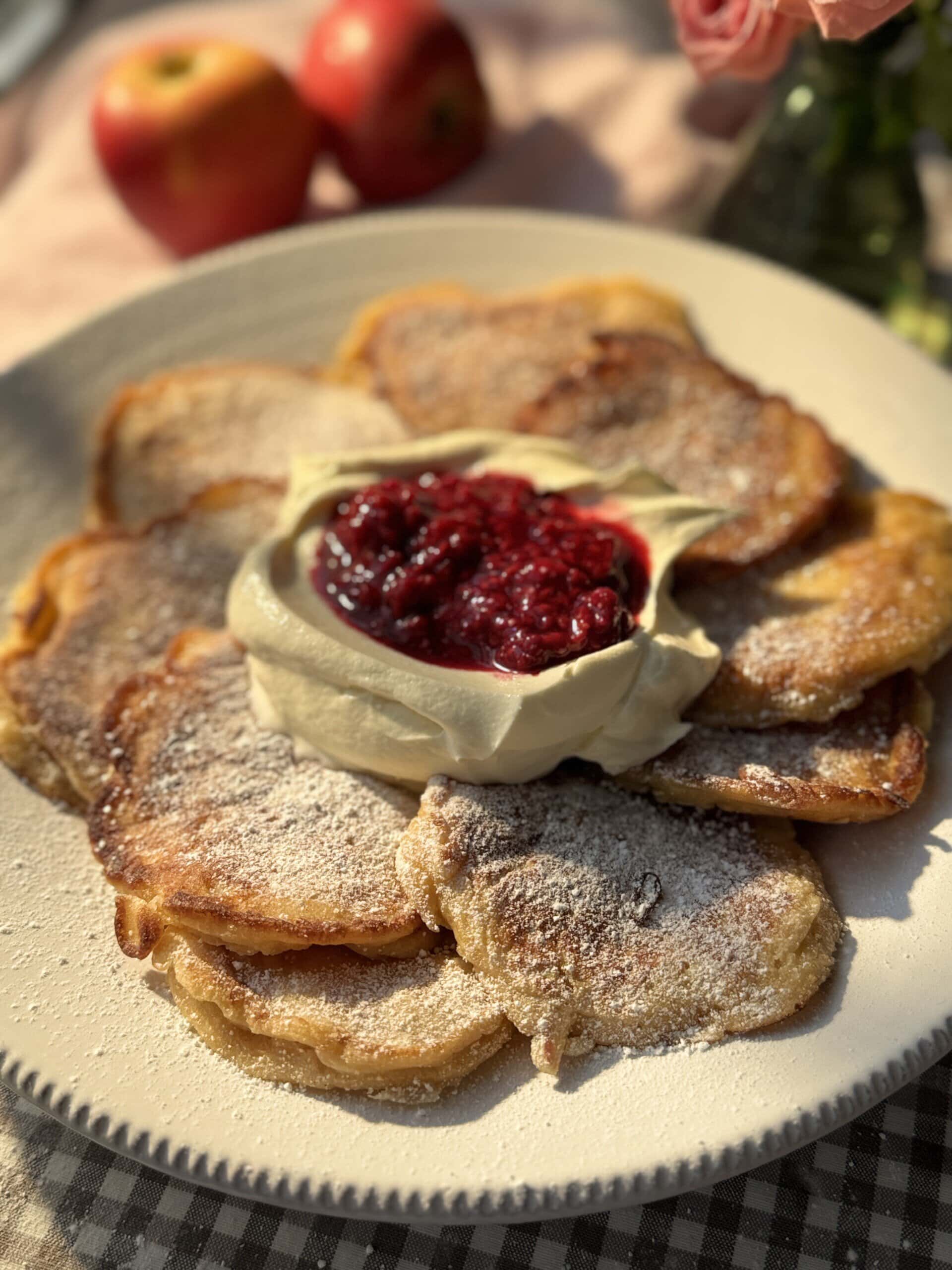 racuchy on a white plate with raspberry compote and whipped cream.