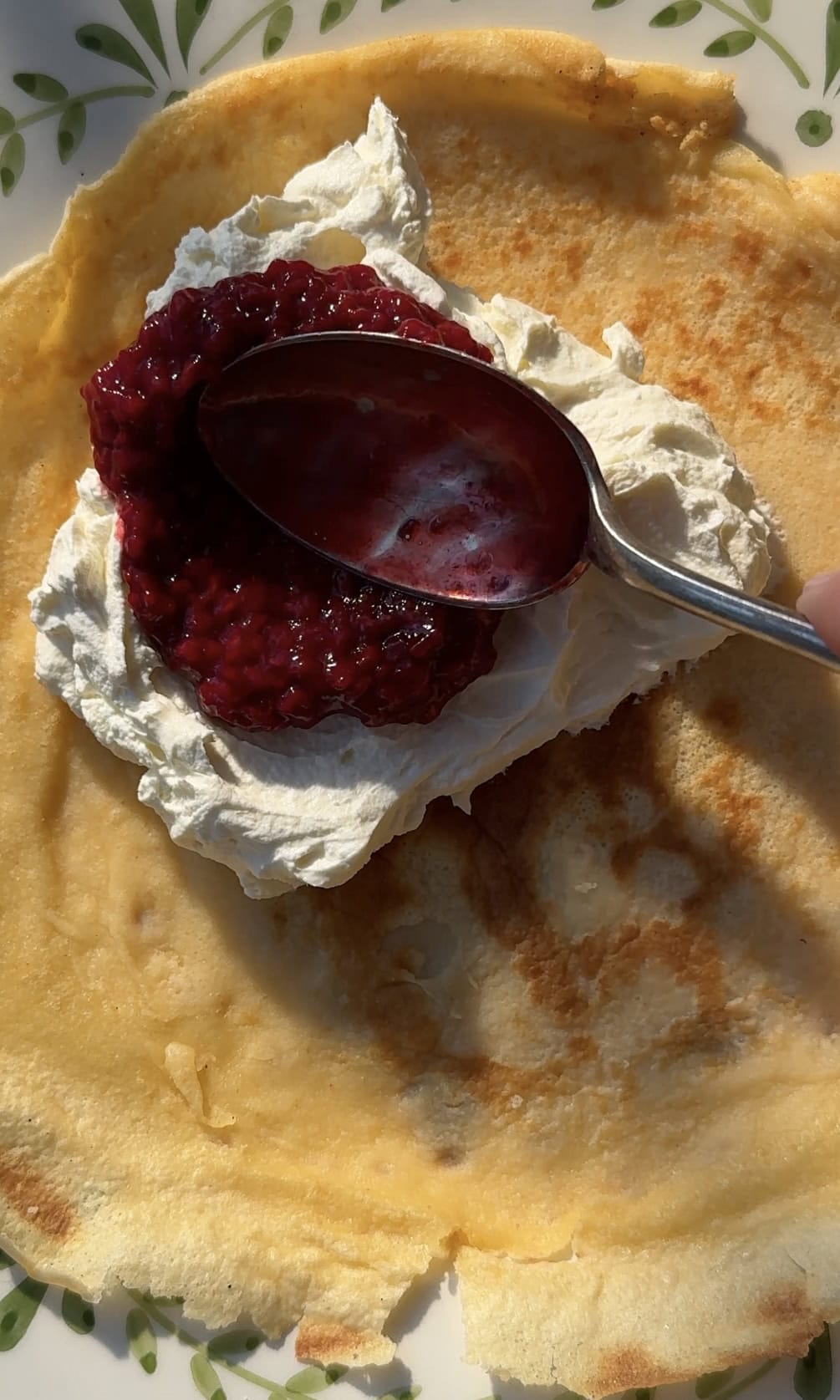 adding cheesecake cream and berry coulis to crepes.