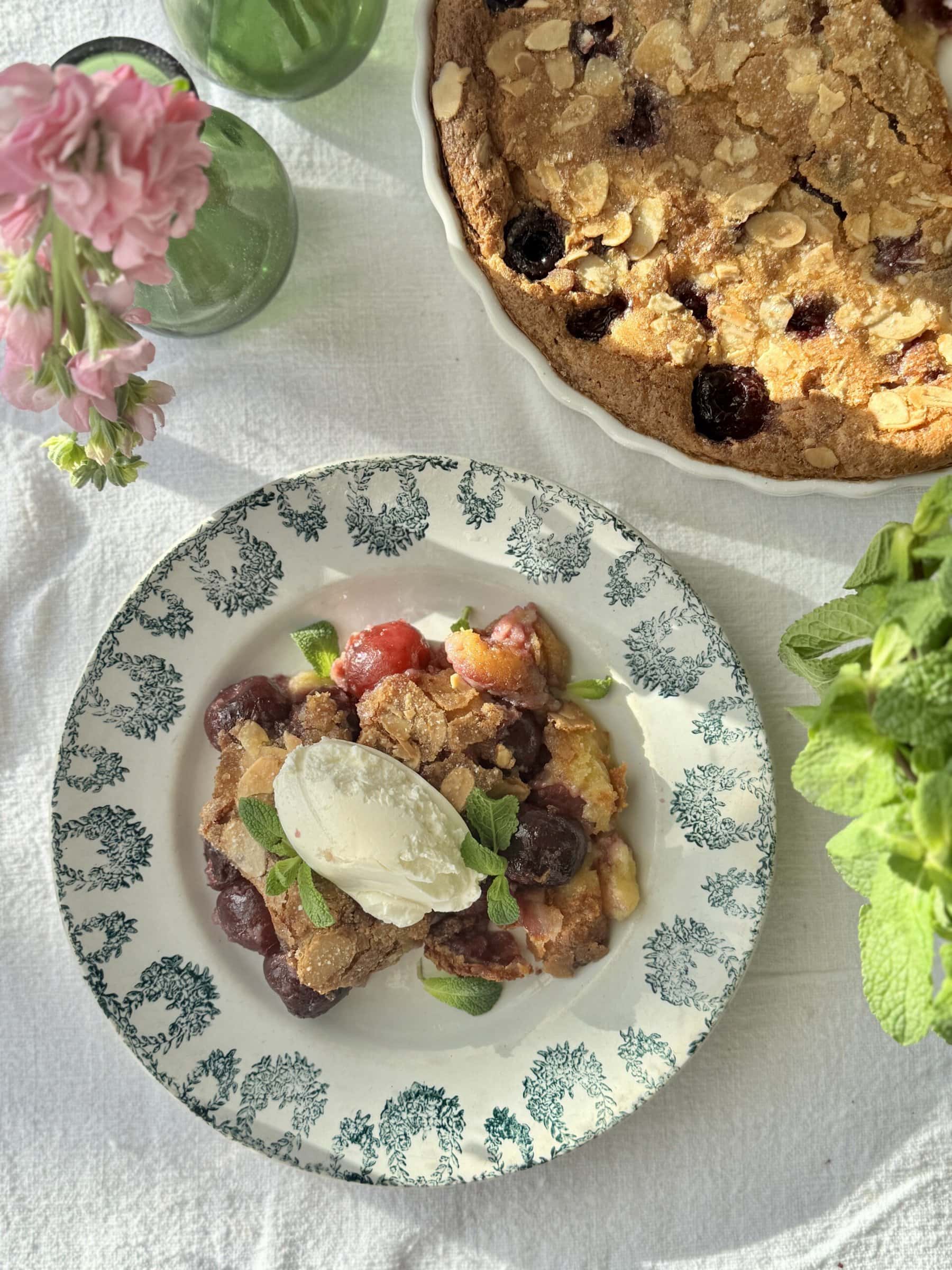 clafoutis aux cerises in a bowl with mascarpone on top and more fresh cherries.