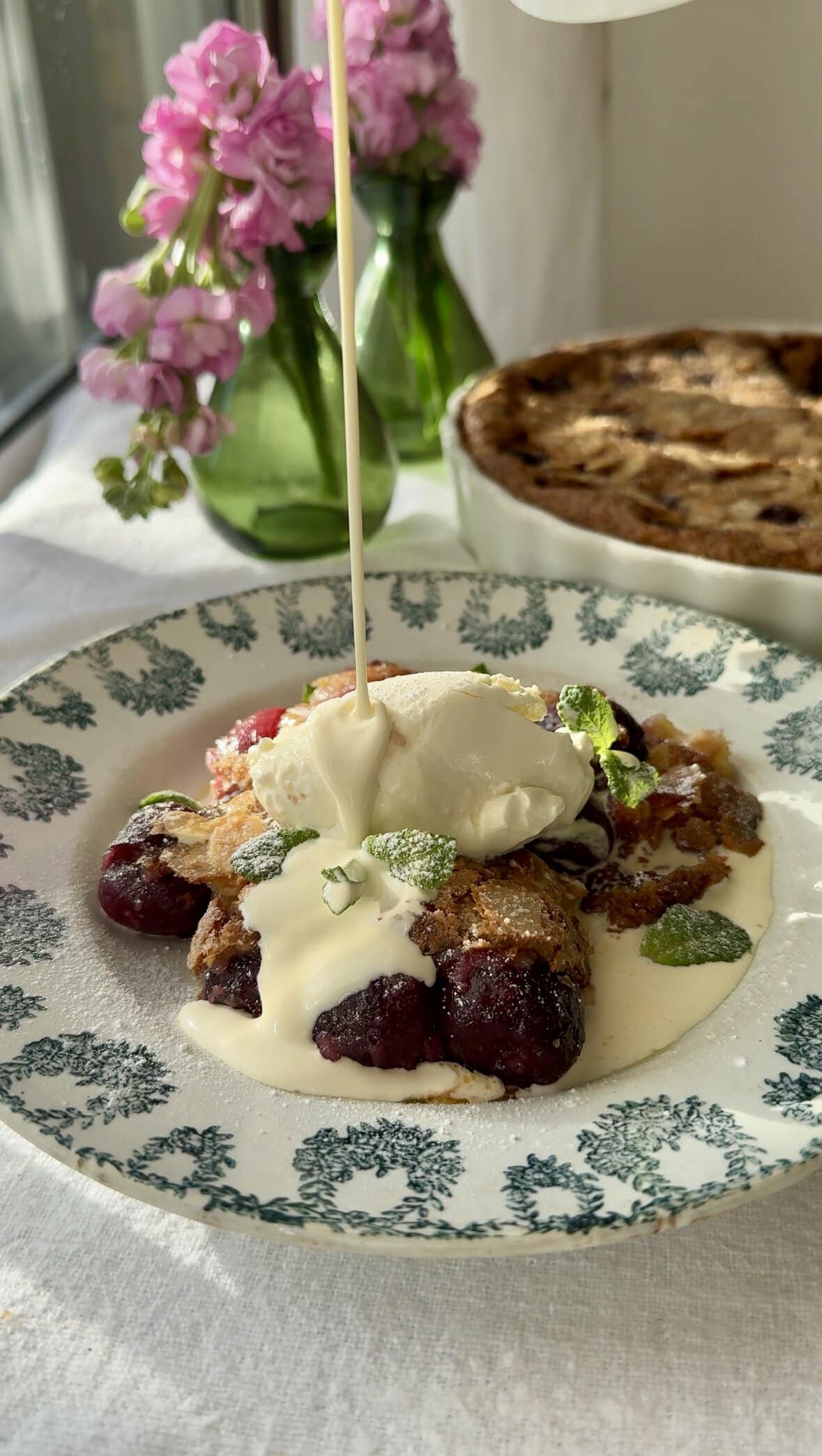 clafoutis aux cerises in bowl pouring cream over the top.