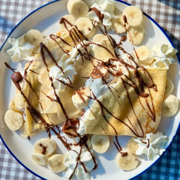 banana crepes on white plate with whipped cream and nutella.